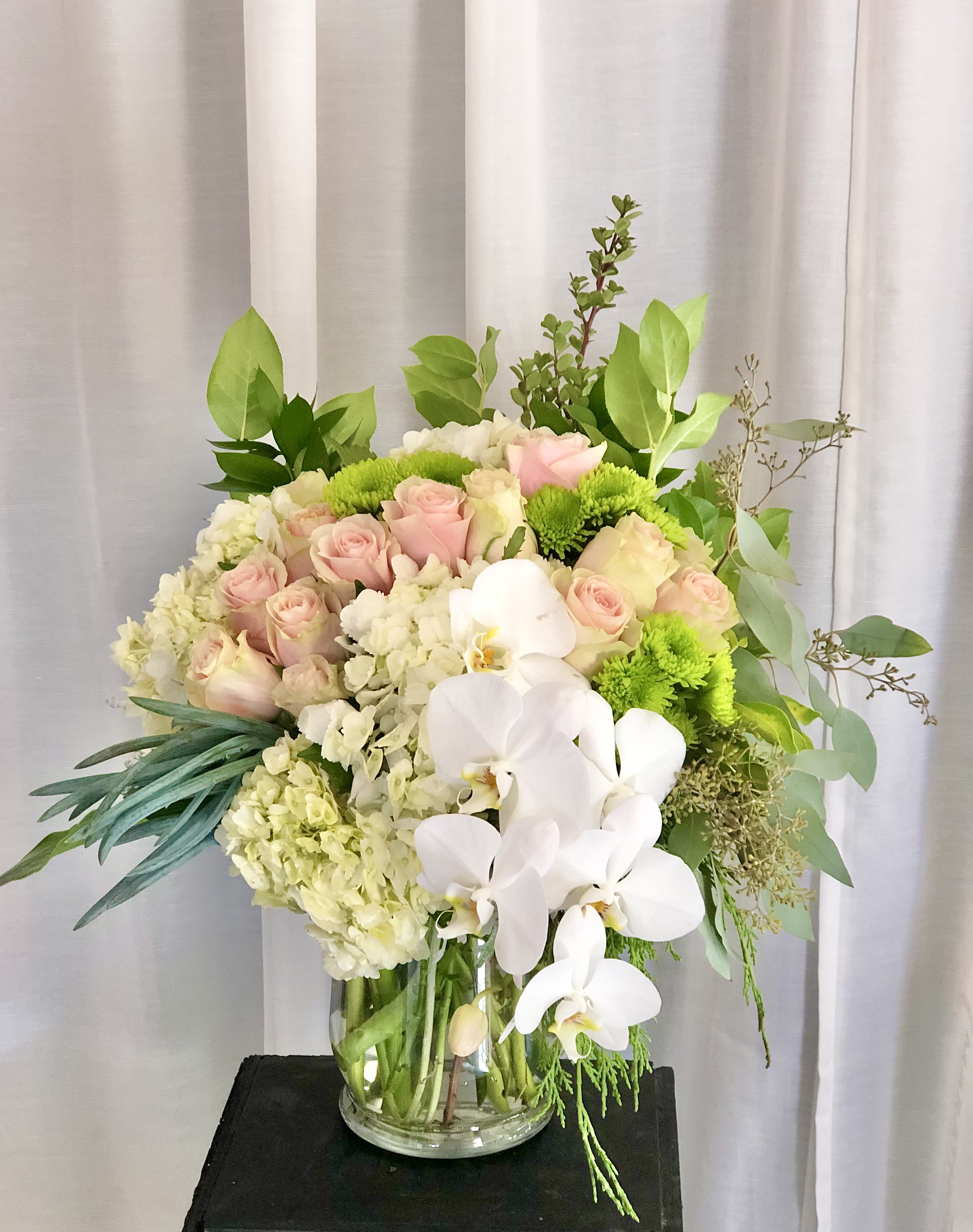 Through the Garden Glass - A beautiful and light mixed arrangement of pale pink roses, white hydrangeas, pompon greens, and white orchids, with green leaf and succulent accents. This floral arrangement flows just like a garden. 