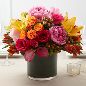 Absolute Love Color Mix - Absolute Love Color Mix Arrangement is a bright and beautiful centerpiece set to bring color and life to your wedding reception. Fuchsia roses light pink roses orange parrot tulips hot pink mini calla lilies orange LA Hybrid Lilies orange spray roses and hot pink spray roses are gorgeously arranged in a clear glass cylindrical vase showcasing ti leaves around the stems to give it a fresh and alluring look.
