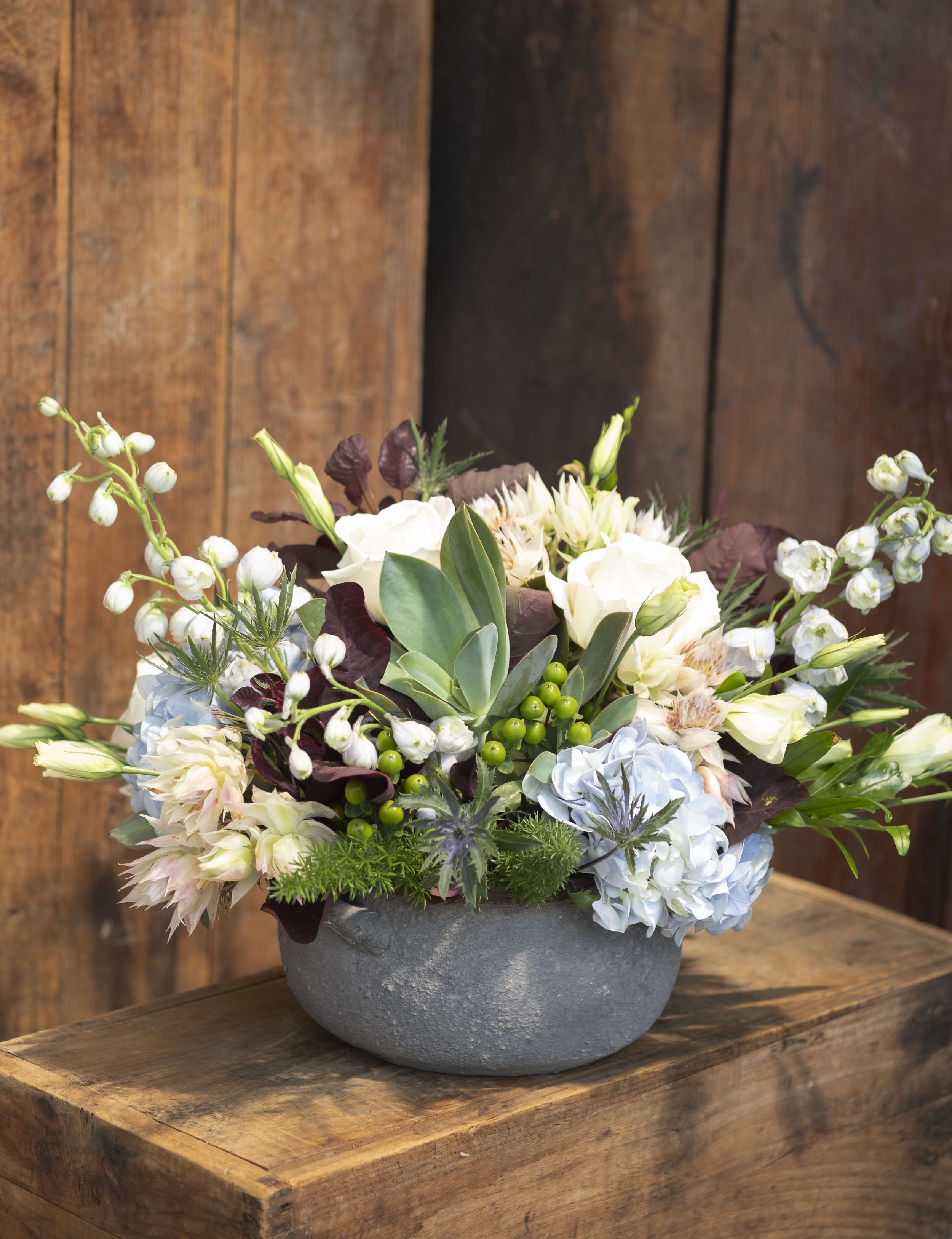 Shades of Blue in a Bowl  - Our artisan handmade arrangement's overall theme is monochromatic with blues and whites.  The actual bouquet or arrangement may not precisely match the photo,but its temperament will. The freshest, artisan flowers available are used to create an exquisite arrangement especially for you. We also use a variety of unusual greenery for an example eucalyptus, salal (lemon leaf), pittisporum. Occasionally, substitutions of flowers or containers happen due to weather, seasonality and market conditions which may affect availability. If this is the case with the gift you've selected,we will ensure that the style, theme and color scheme of your arrangement is preserved and will only substitute items of equal or higher value.