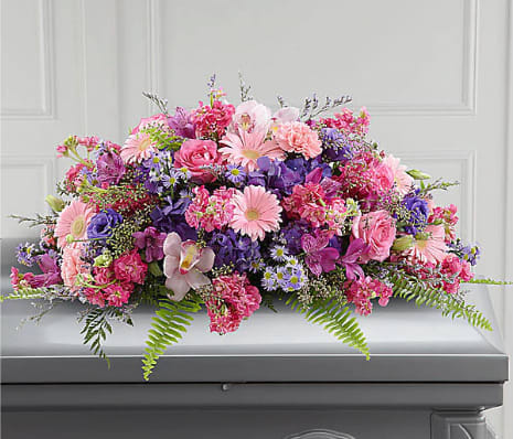 Glorious Garden™ Casket Spray - Colorful, full and lush, this extraordinary casket spray makes a memorable and touching statement of sympathy that’'s sure to be a comfort to grieving family and friends. This vibrant mixed flower casket spray is a generously scaled floral creation of bright and blue spring color includes pink carnations, cymbidium orchids and gerbera daisies, hot pink roses and stock, purple hydrangea and lisianthus, lavender alstroemeria, Monte Casino and limonium all accented with lush greens. It’'s made to fit over the closed portion of a casket cover during visitation at a funeral home, at a funeral service and at a graveside ceremony at the cemetery. Spray approximately 14&quot;H x 29&quot;W. 
