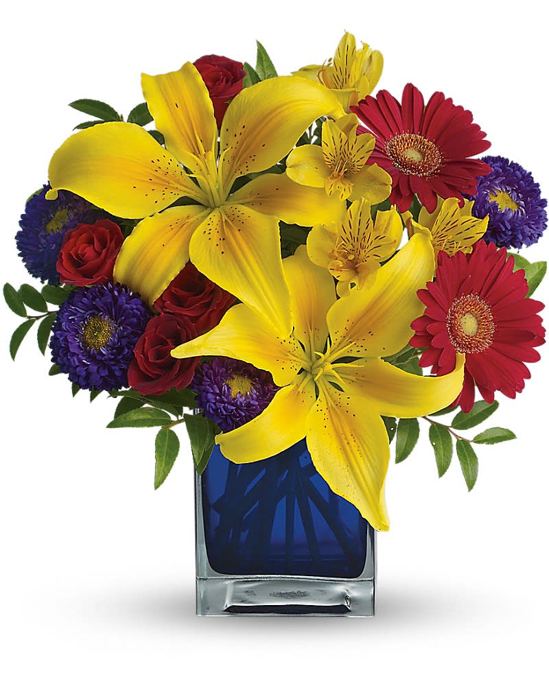 Teleflora's Blue Caribbean - Standard - 13&quot; H x 12&quot; W Deluxe - 13 1/2&quot; H x 12 1/2&quot; W Premium - 14&quot; H x 13&quot; W  Martinique St. Maarten any tropical paradise is the perfect setting for this explosively colorful bouquet in a chic blue contemporary cube vase. Can't go just now? Bring the island home. The exciting bouquet includes yellow Asiatic lilies red miniature gerberas purple Matsumoto asters red spray roses and yellow alstroemeria accented with fresh greenery. Delivered in a blue contemporary glass cube vase.