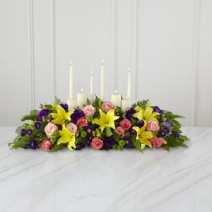 The Forever Arrangement - This inspirational altar piece makes an inspired contribution to a funeral service – one that truly shows how much you care. Handcrafted with peach and coral roses, purple lisianthus, asters, yellow asiatic lilies and lush green accents in a long low arrangement it makes a natural setting for a variety of candles (included). As an accompaniment to a funeral it’s an excellent choice for most services both elaborate and simple.
