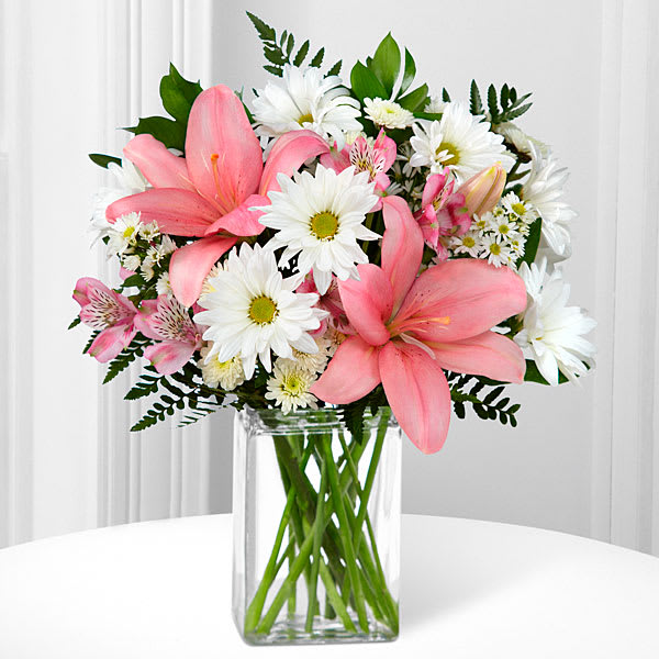 In the Presence of Pink - This bouquet includes the following: pink LA Hybrid Lilies, white traditional daisies, white monte casino asters, white chrysanthemums, and an assortment of lush greens arranged in a clear glass vase.
