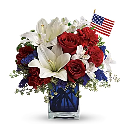 America the Beautiful - Red roses, white asiatic lilies, white alstroemeria, blue statice and red carnations are gathered with green pitta negra, seeded eucalyptus and a small American flag in a cobalt blue glass cube. A perfect gift for Memorial Day, Fourth of July, Veterans' Day, or to honor a loved one who served for our country.