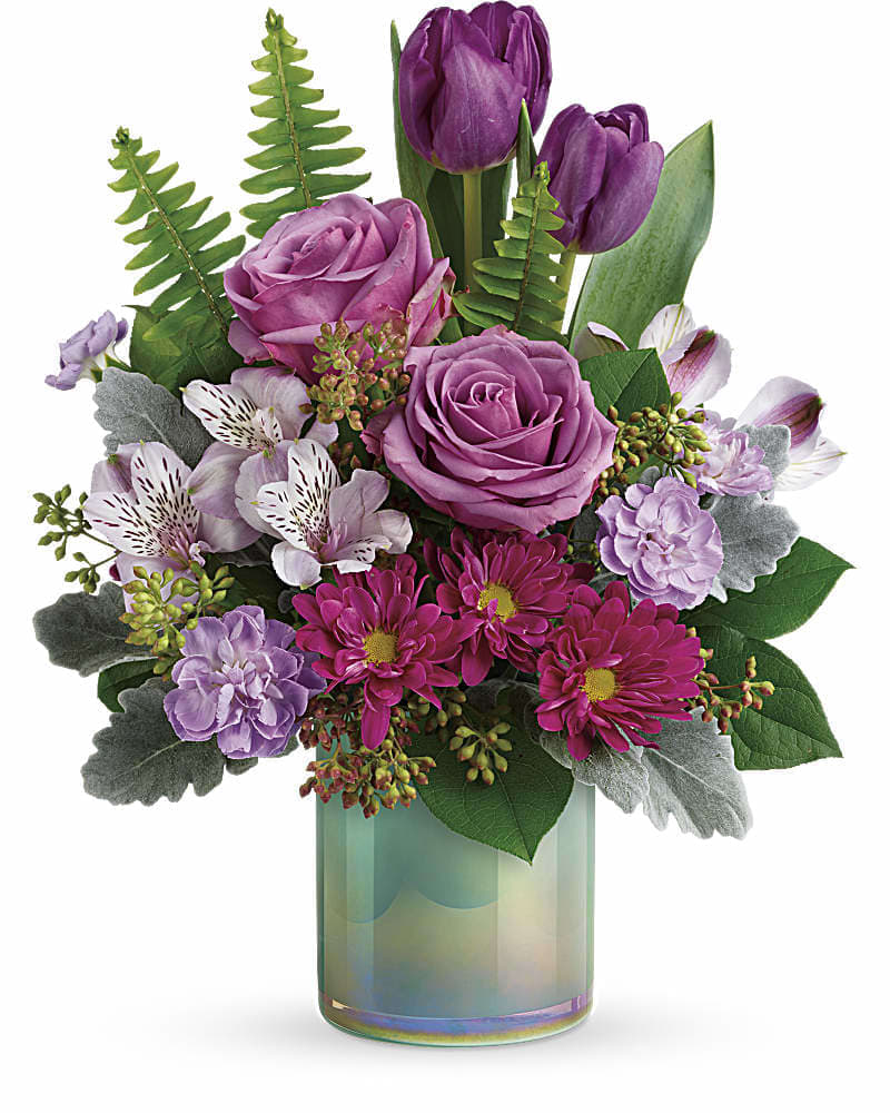 Teleflora's Art Glass Garden Bouquet - The art of affection! This glorious, iridescent aqua blue glass vase brings contemporary beauty to this lush lavender bouquet of roses, tulips and alstroemeria! This artistic arrangement features lavender roses, purple tulips, lavender alstroemeria, lavender miniature carnations, purple daisy spray chrysanthemums, dusty miller, seeded eucalyptus, sword fern, and lemon leaf. Delivered in an Art Glass Garden Cylinder.