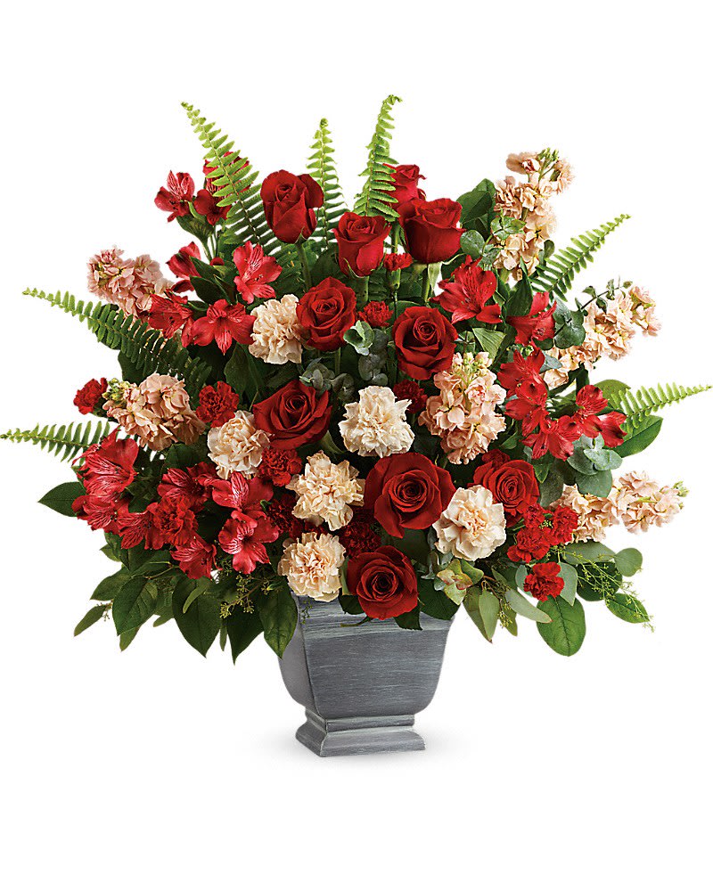 Teleflora's Bold Tribute Bouquet - A bold expression of your deepest condolences, this elegant mix of red and peach blooms in a large antiqued pot brings strength and comfort. Red roses, red alstroemeria, peach carnations, miniature red carnations, and peach stock are arranged with spiral eucalyptus, seeded eucalyptus, sword fern, and lemon leaf. Delivered in a Modern Heritage pot.