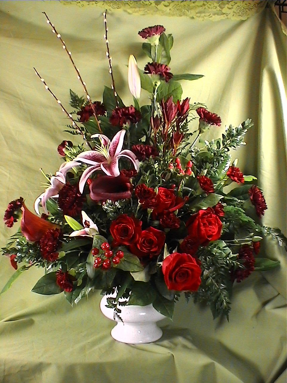 Garnet Sympathy Vase - Pay tribute with this stunning sympathy vase. Assorted varieties of red roses and florals are highlighted with Stargazer Lilies, Pussy Willow Branches and Hypercum Berries. Flower varieties and container may vary depending on availability and season.