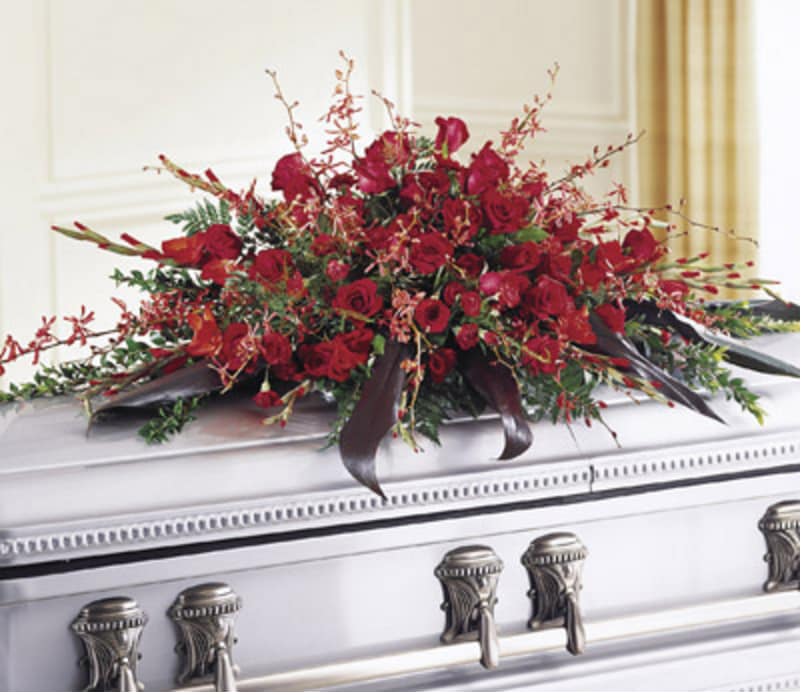 Deeply Adored Casket Spray - An abundance of deep red roses and delicate orchids enrich this elegant casket spray to bid a farewell to one who is truly adored. Arranged on a bed of greenery with varying textures.