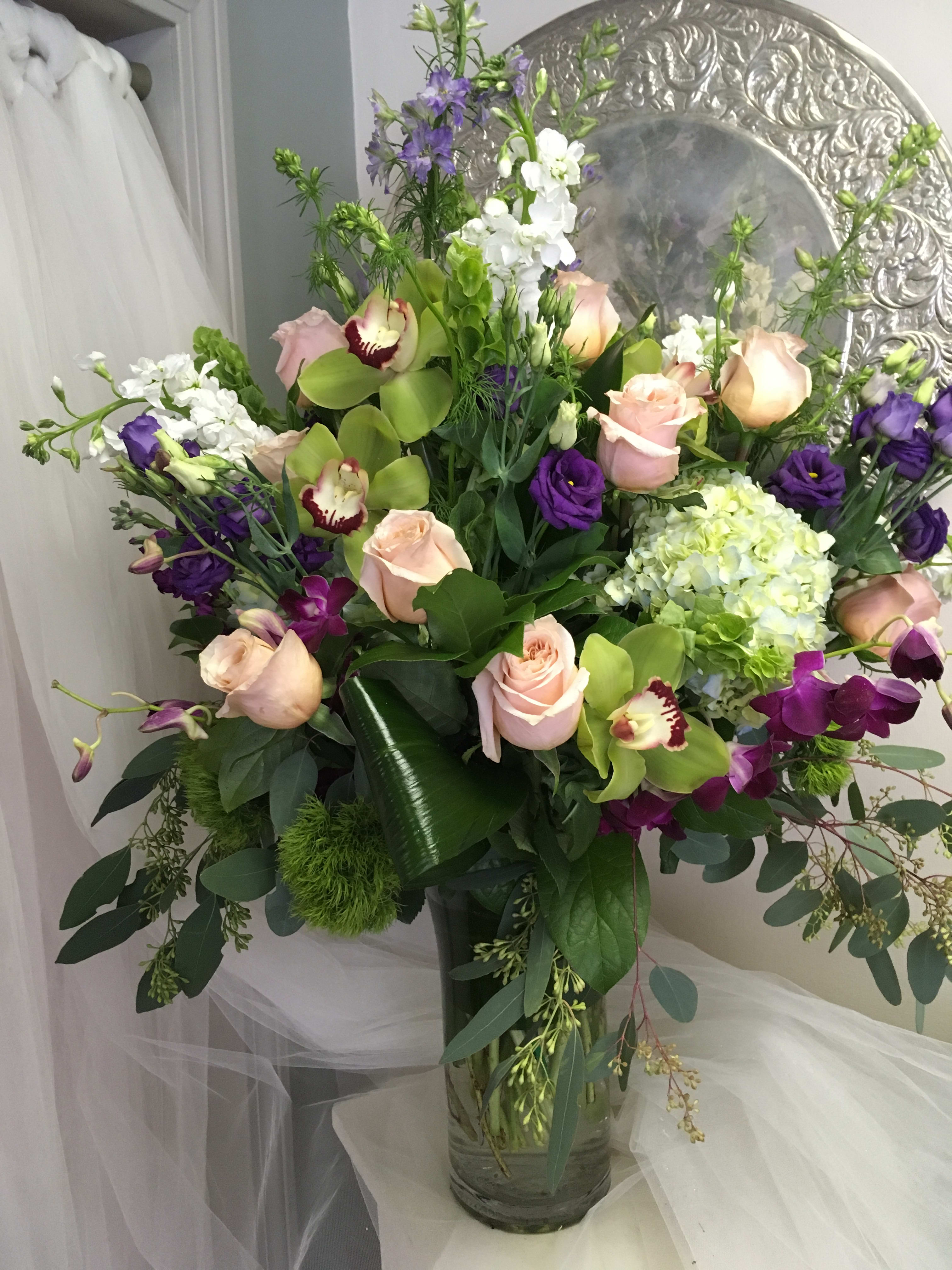 Always You - This is a stunning display of a mix of peach roses, orchids , purple lisianthus, stock and larkspur. It is sure to make one pause as they walk by.  A custom piece that is genuinely a showstopper. 