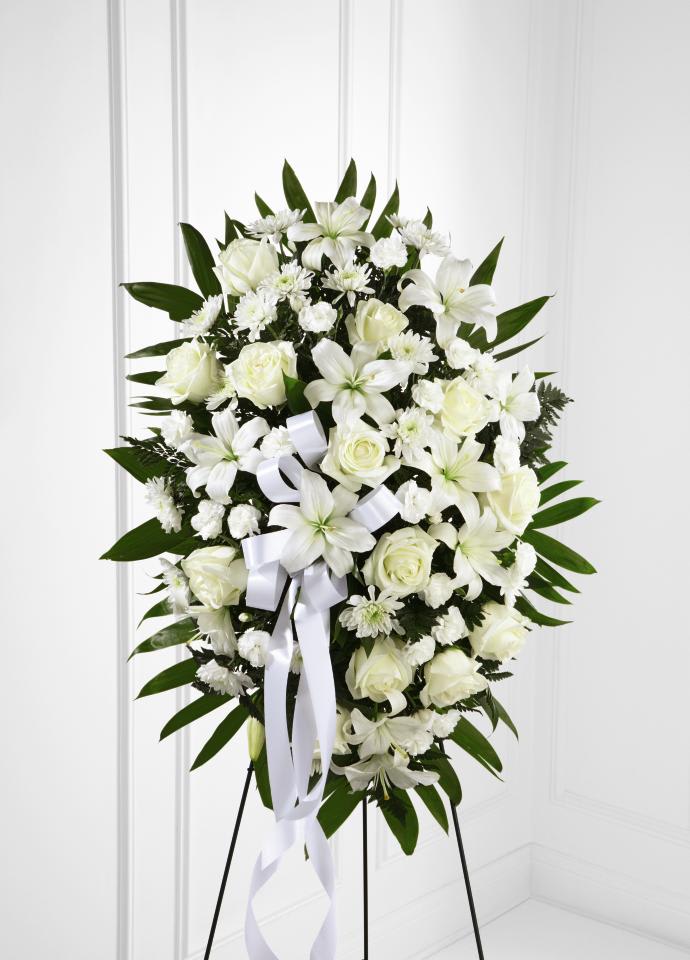 Exquisite Tribute Standing Spray - Exquisite Tribute Standing Spray is an elegant display of  sweet serenity. White roses, Asiatic lilies, chrysanthemums and mini  carnations are artfully arranged amongst emerald palm fronds and lush  greens. Accented by white satin ribbon and standing on a wire easel,  this standing spray is an outstanding way to honor the life of your  loved one.