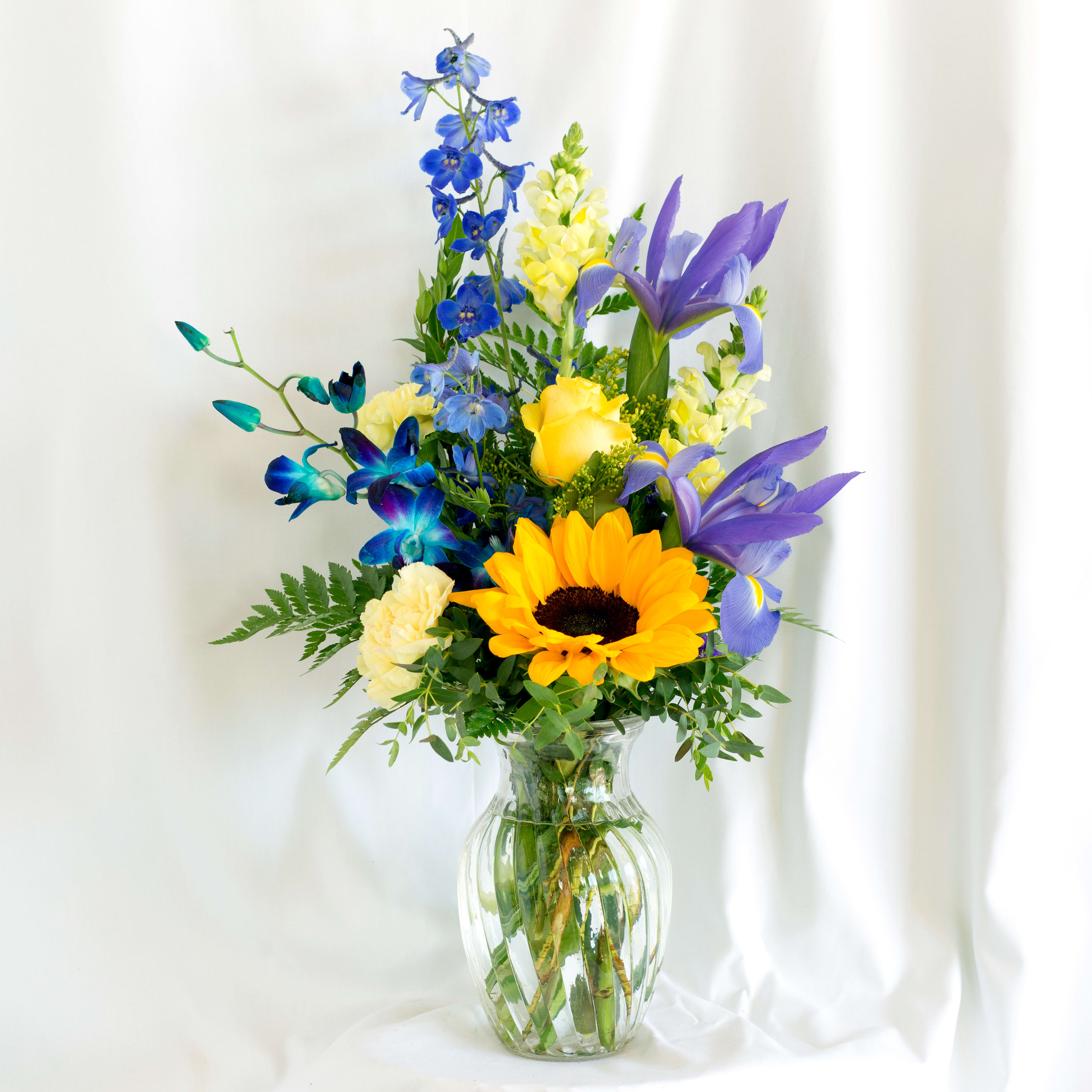 Yellows and blues - Mixed seasonal flowers in yellows and blues in a clear vase, perfect for any occasion.