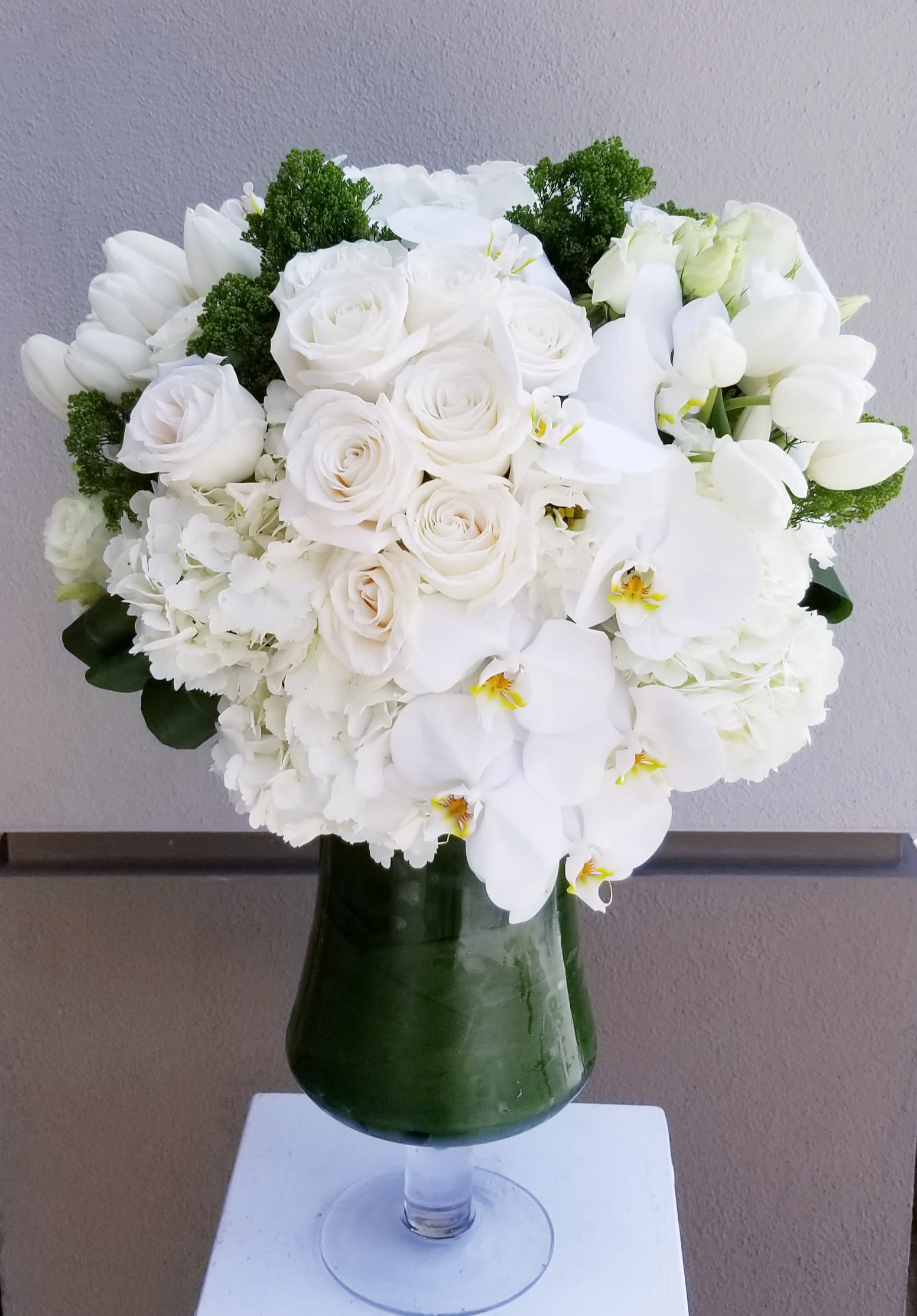 Blanca Blanca - Elegant arrangement in glass urn of all white premium blooms.It includes hydrangeas, roses, tulips and phalaenopsis orchids.