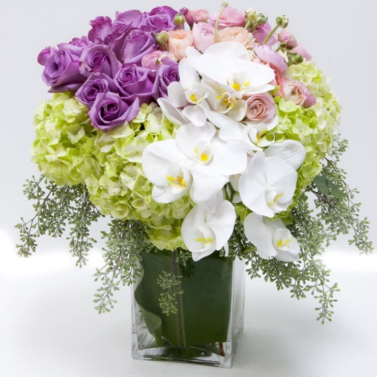 Roses Orchids and Hydrangeas - A timeless design for the modern age of purple roses, orchids and pink blossoms celebrated in a statuesque clear glass vase