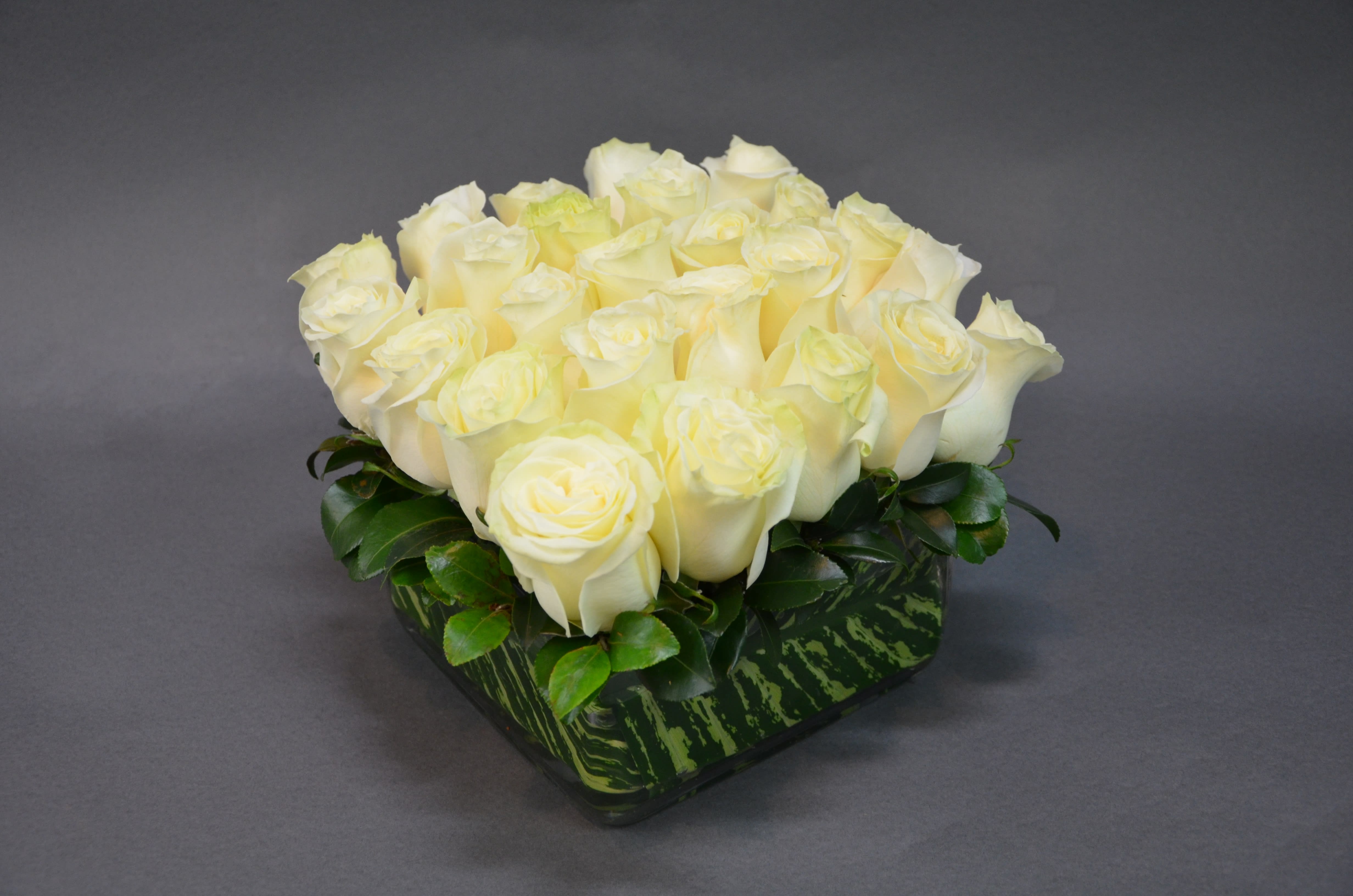 Perfectly Paired  - For Those who Seek to Illuminate their World  with Pure Extraordinary Beauty, White Never Fails to Exceed Expectations.  Pristine White Roses in a Clear Glass Rectangular Vase Accented with Glossy Foliage    