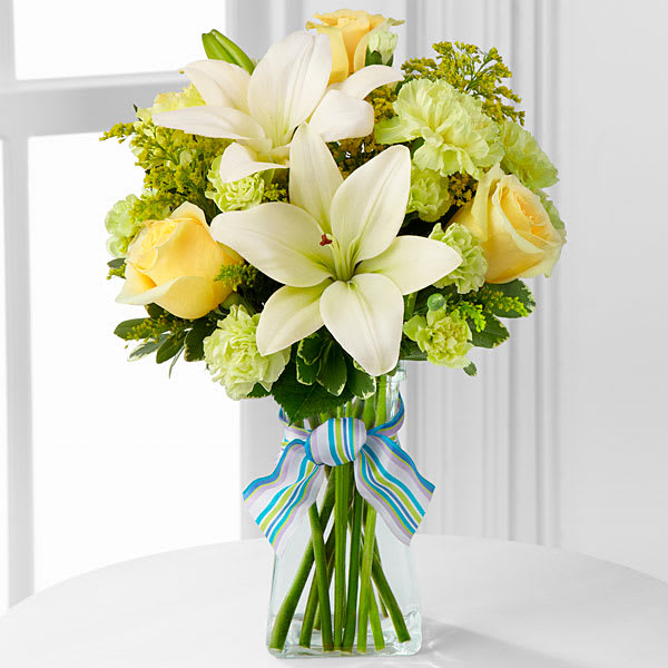 The FTD Boy-Oh-Boy Bouquet - The FTD® Boy-Oh-Boy™ Bouquet employs roses and Asiatic lilies to send your bright and sunny congratulations on the birth of their new baby boy! Yellow roses and carnations are brought together with pale green mini carnations white Asiatic lilies yellow solidago and lush greens exquisitely arranged in a clear glass gathered square vase. Accented with blue and lavender wired ribbon this bouquet creates a wonderful way to send your warmest wishes for the adventure of parenthood ahead.  **Lilies may arrive in bud stage.**