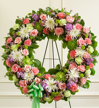 Serene Blessings Pastel Standing Wreath - This beautiful floral tribute shows your compassion, faith and love during this difficult time. This standing spray arrangement in the shape of a wreath is created from fresh mix roses, white football mums, spiral eucalyptus and more. Traditionally sent directly to the funeral home by family members or friends and displayed on a stand. 