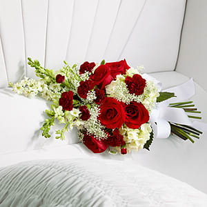 The FTD Forever in Our Hearts Casket Adornment - The FTD® Forever in Our Hearts™ Casket Adornment is a beautiful accent piece that adds that extra touch of elegance to their final farewell service. Red roses and mini carnations are eye-catching and bright arranged amongst white hydrangea larkspur snapdragons and Queen Anne's Lace. Tied together with a white grosgrain ribbon this gorgeous bouquet is a lovely way to say goodbye to your beloved.