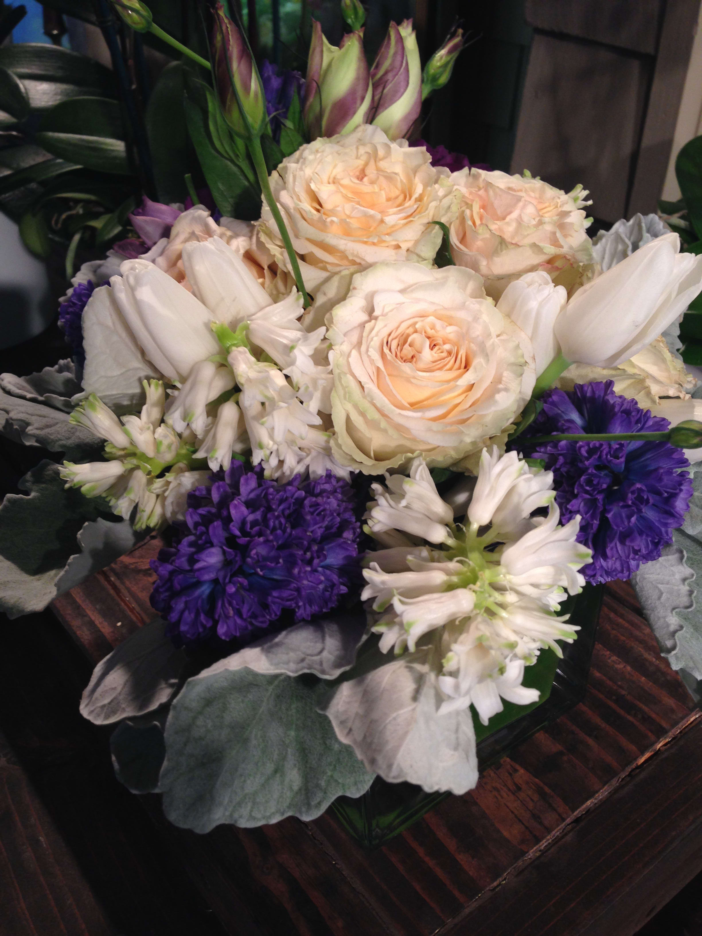 Green Sahara - Mix of sahara roses, purple and white hyacinth, lisianthus, premium fillers, arranged in a glass square vase wrapped in fresh banana leaves.