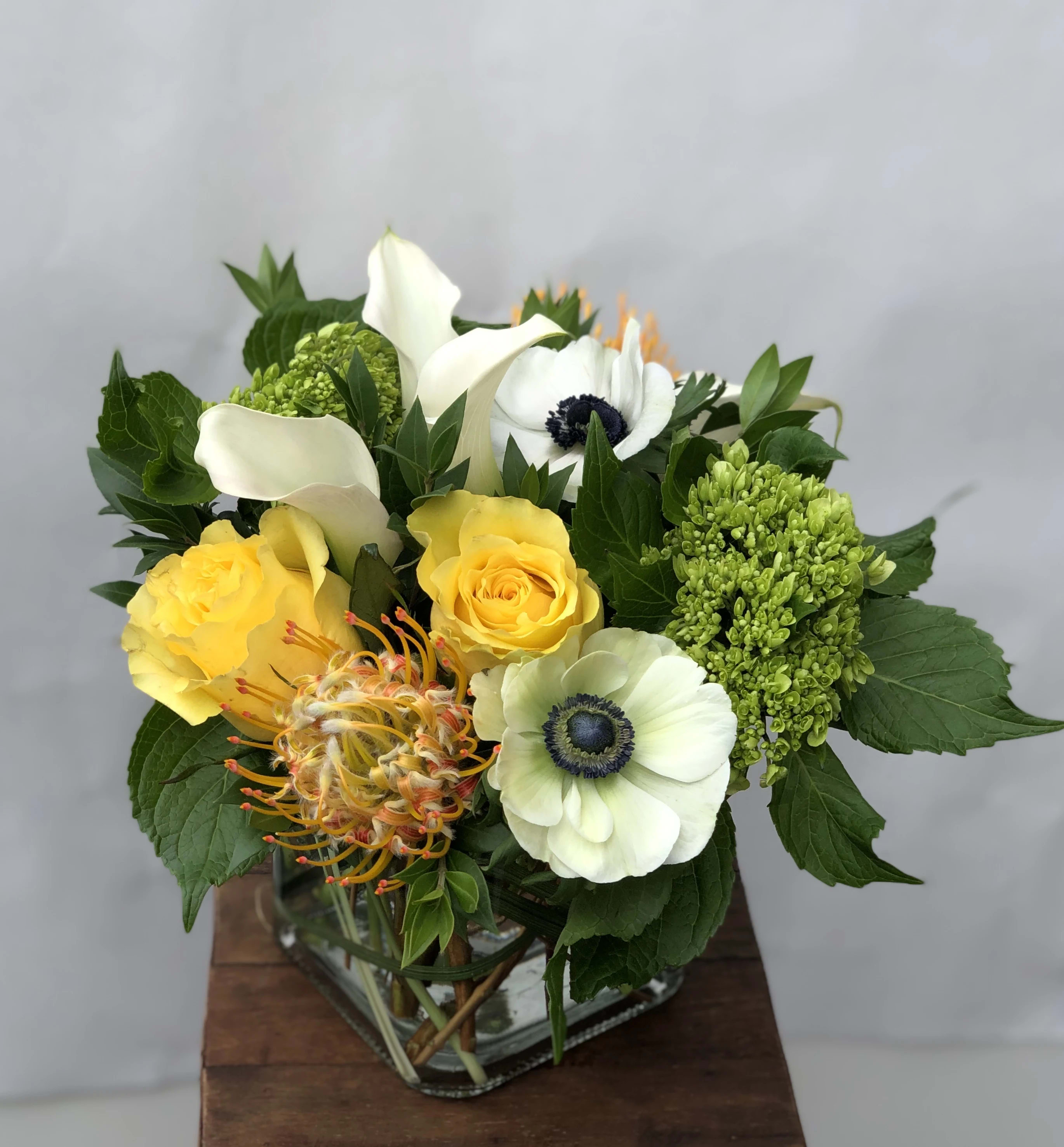 Protea Perfection - This arrangement features stunning pincushion proteas, mini green hydrangea, white anemones, yellow roses and callas.