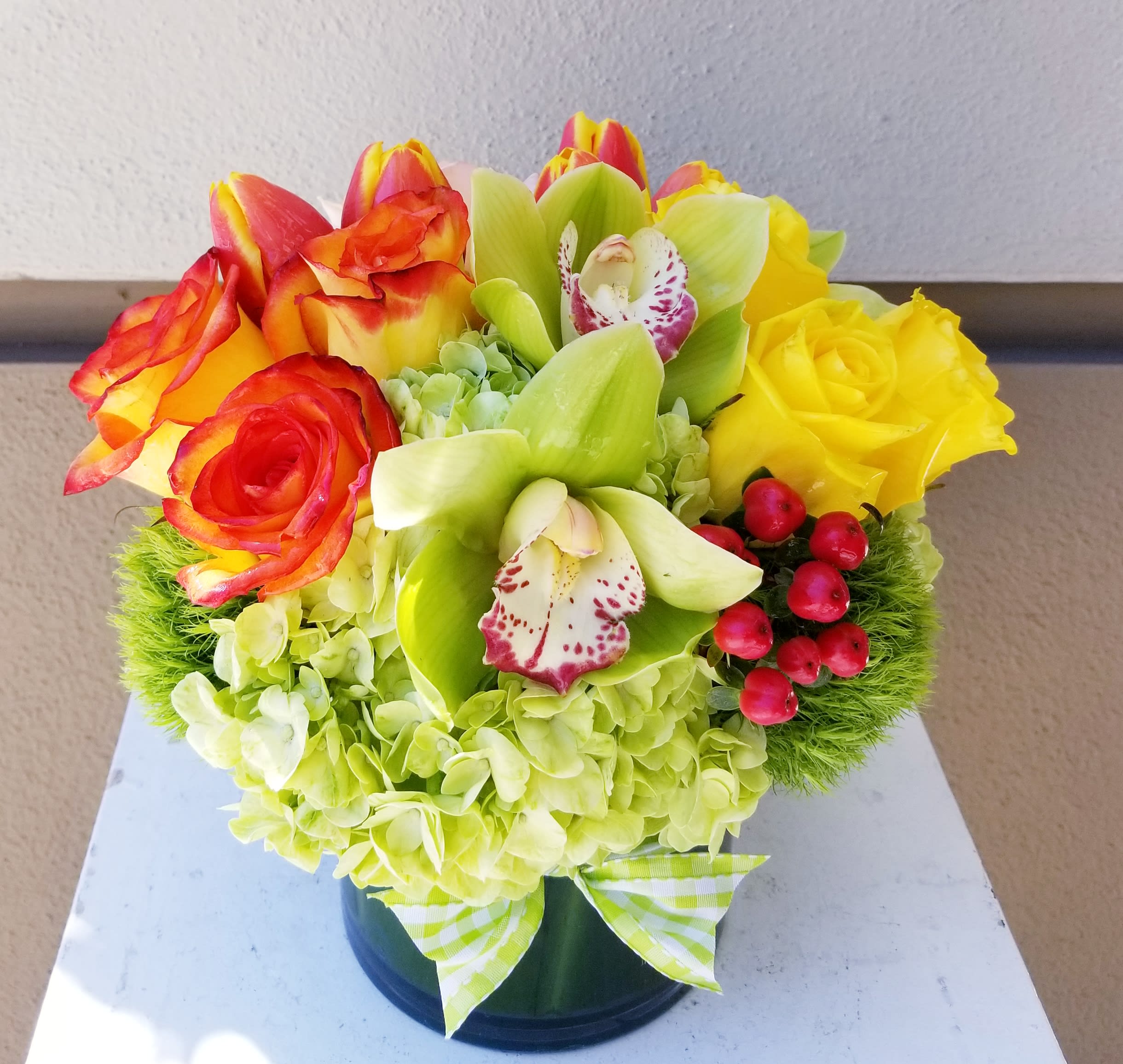 Zest - Low Cylinder composed of green, orange and yellow blooms such as roses, hydrangeas, orchids and tulips.
