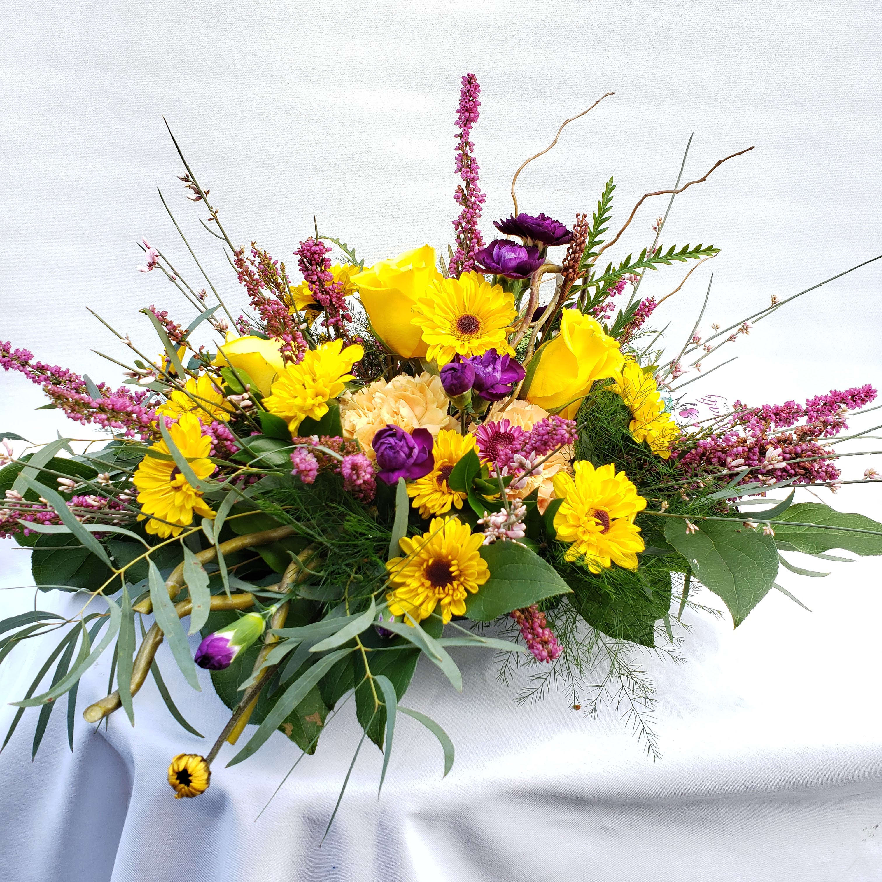 A little bit of Sunshine - This bouquet reminds me of the sunset with the pinks, yellows, and purples.  The flowers in this arrangement are yellow viking daisy, yellow roses, peachy carnations, purple mini carnations, and pink heather.    To take care of this arrangement is easy: it comes in a standard green tray and everyday just adds a little water. These flowers are long lasting and will do well in any room, just not in direct sunlight.   