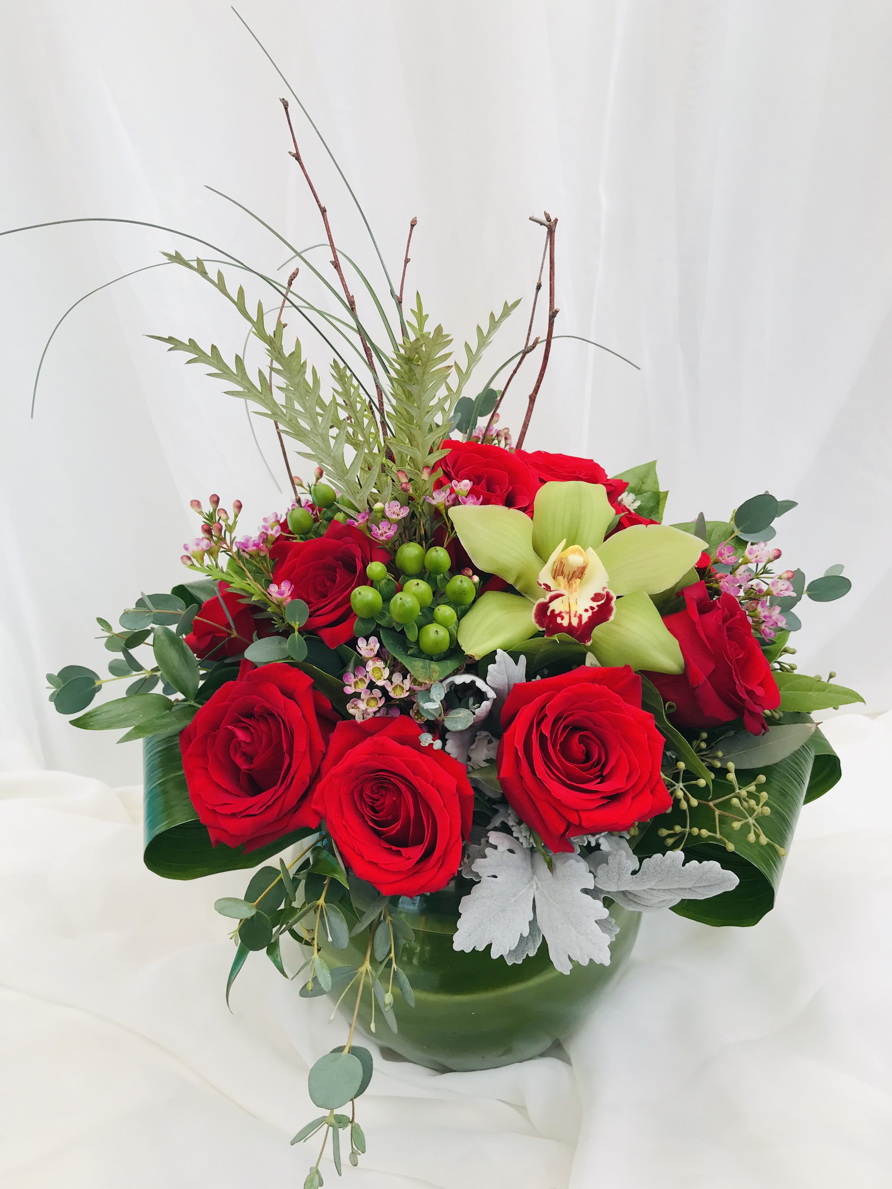 &quot;Loving You Is Easy&quot; Flowers - This gorgeous Valentine's Day arrangement consist of a dozen red roses and orchids with an abundance of high class greenery including dusty miller and eucalyptus. It is the perfect piece to give to your significant other this season.