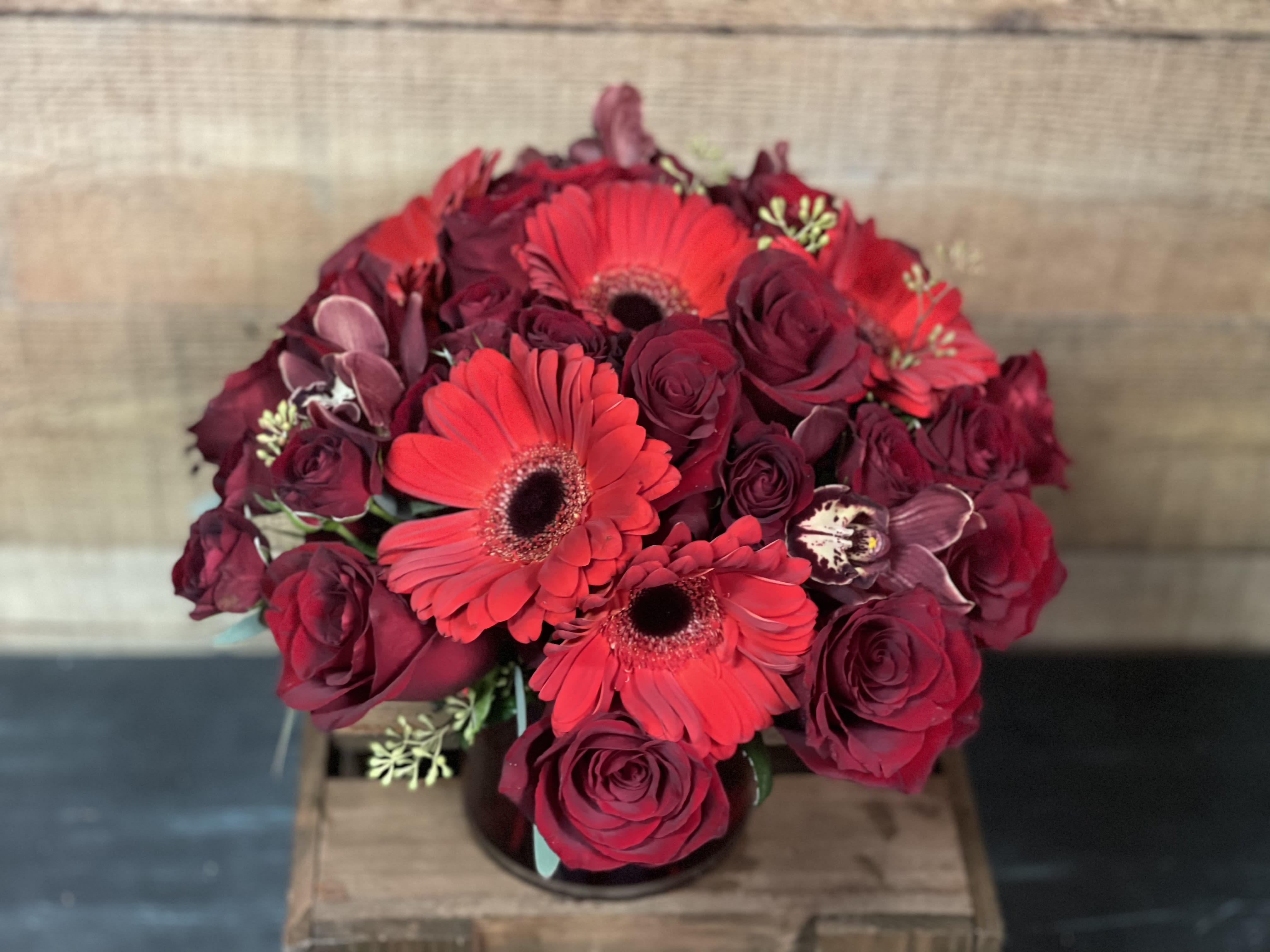 Lady In Red - Red Roses, Red Gerbera Daisies, and Burgundy Cymbidium Daisies make up this one of a kind arrangement