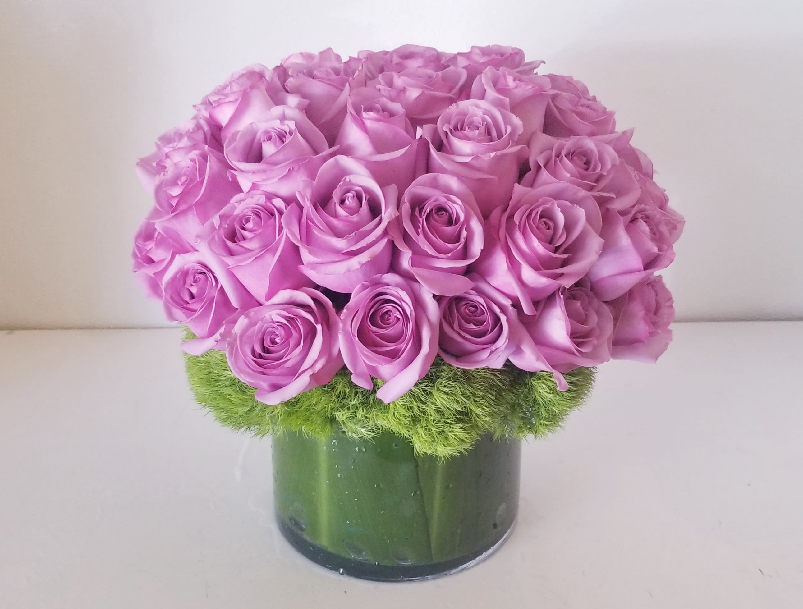 Devotion - Contemporary design of all lavender roses designed in a low glass cylinder lined with green t-leaf.