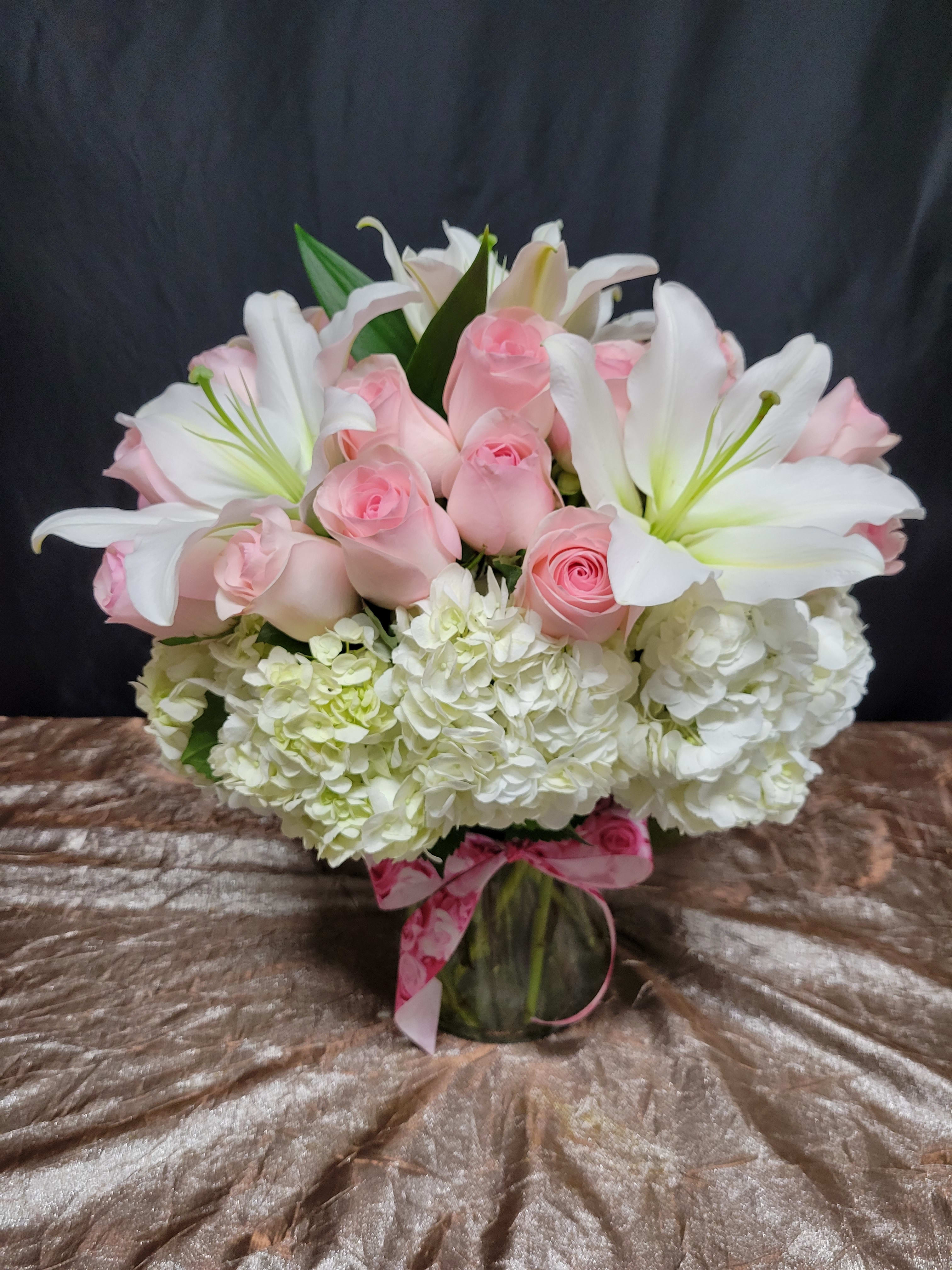 Delicate Romance - This centerpiece creates a romantic atmosphere with blush roses, fluffy white hydrangeas, lisianthus, and various dancing greeneries.  