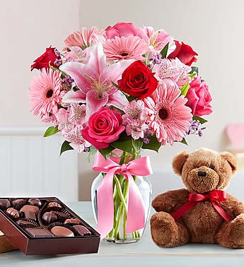 Valentine Surprise - Arrangement of red and hot pink roses, pink Stargazer lilies, pink Gerbera daisies, pink alstroemeria, pink limonium and salal Lilies and alstroemeria may arrive in bud form and will open to full beauty in 2-3 days. In a clear glass vase decorated with a pink ribbon.Paired with a plush bear and 8 oz. box of delicious assorted chocolates. *Bear and chocolate assortment may vary due to local availability 