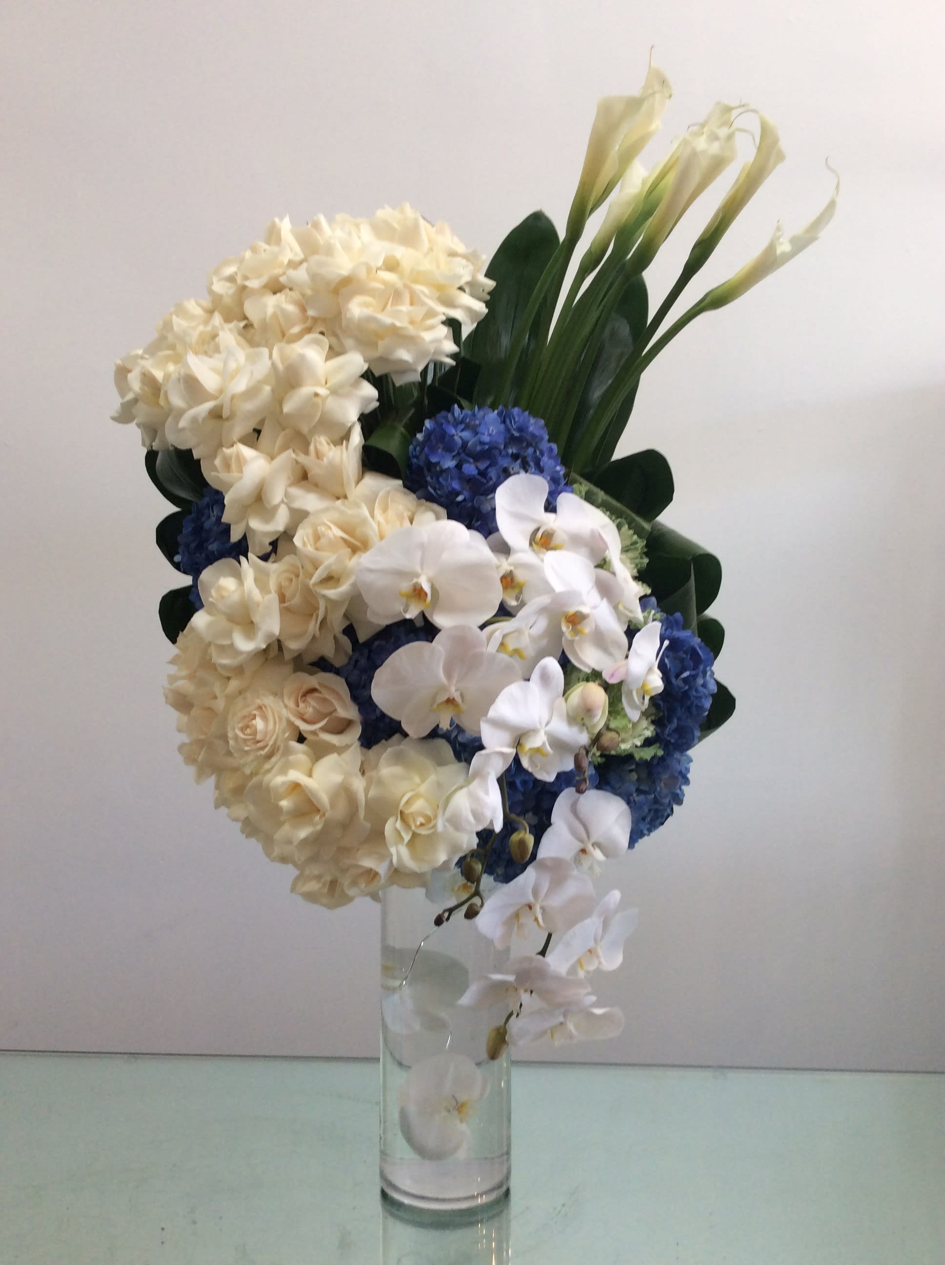 Blue Streak - A dynamic tower of flowers made of cream roses, white callas, phaelenopsis orchids and a blue streak of blue hydrangea. It's sure to impress!