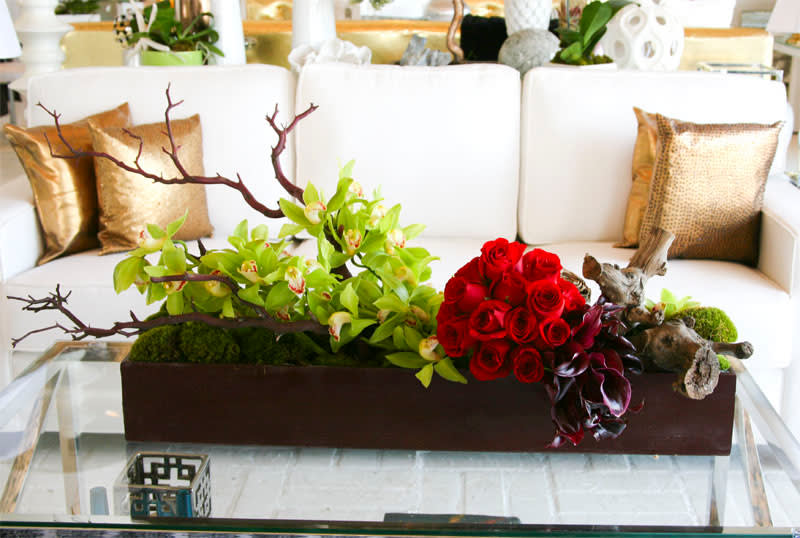 Dark Green - A contemporary display of green cymbidium orchids sitting atop mood moss and with a vibrant pop of red roses, and black calla lilies intertwined with manzanita branches in a sleek wooden box.