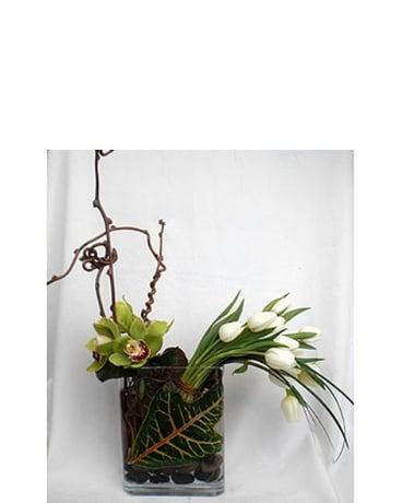 Tulip Delight - Contemporary design of simply white tulips, cymbidium orchids, river rocks in a glass vase lined with a green leaf.  Available in other colors   Product ID: DF-1310