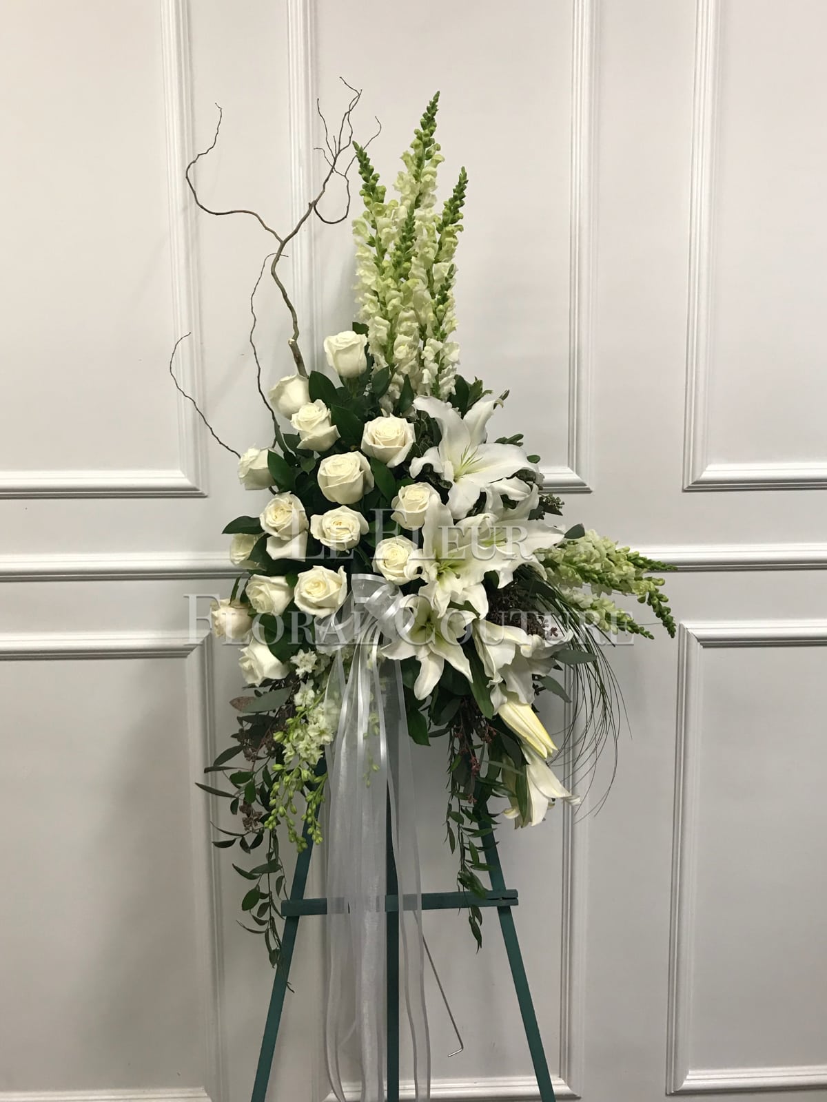 Adorned Condolences - A very unique and beautiful standing spray consisting of white roses, casa blanca lilies and white snapdragons; decorated with curly willow and cascading greens. 