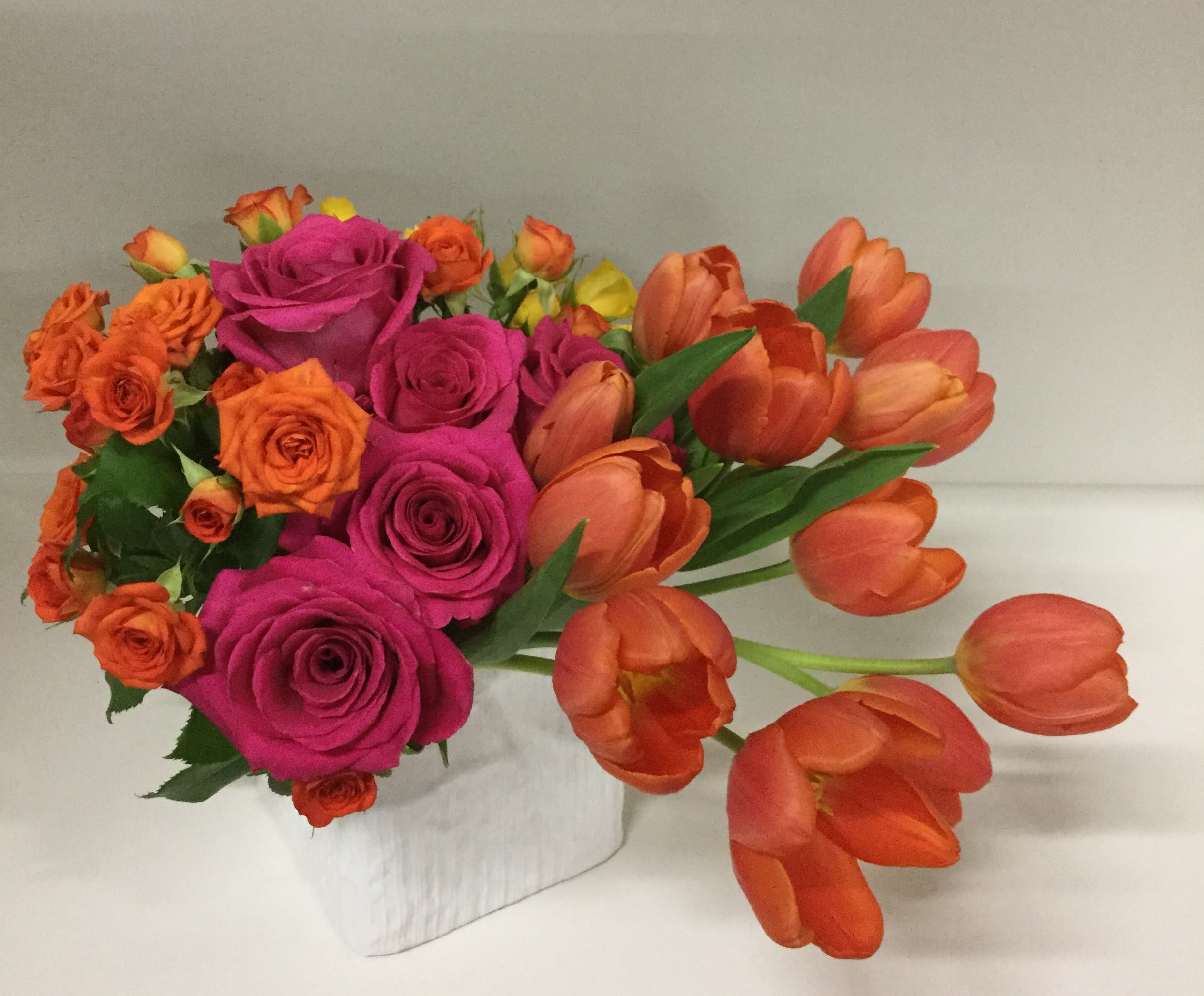 Desert Dawn - This arrangement has a winning combination of color palette and structure of the design. Groupings of hot pink roses, orange spray roses and asymmetrically extending orange tulips, with just a touch of greenery, indeed resembles the dawn colors of Arizona sky. All arranged in a 5”x 5” white satin cube. Approximate dimensions: 9”x 13”