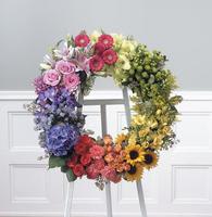 Over the Rainbow - A wreath of mixed colors and textures to create this rainbow. Spray roses, lilies, mums. asters, a hydrangea, carnations, a few sunflowers and other assorted blooms create this wreath. (If you would like a ribbon &amp; wording, i.e., loving friend, Dear Mother, In-Law, Nephew, etc. Please call us for pricing.)   