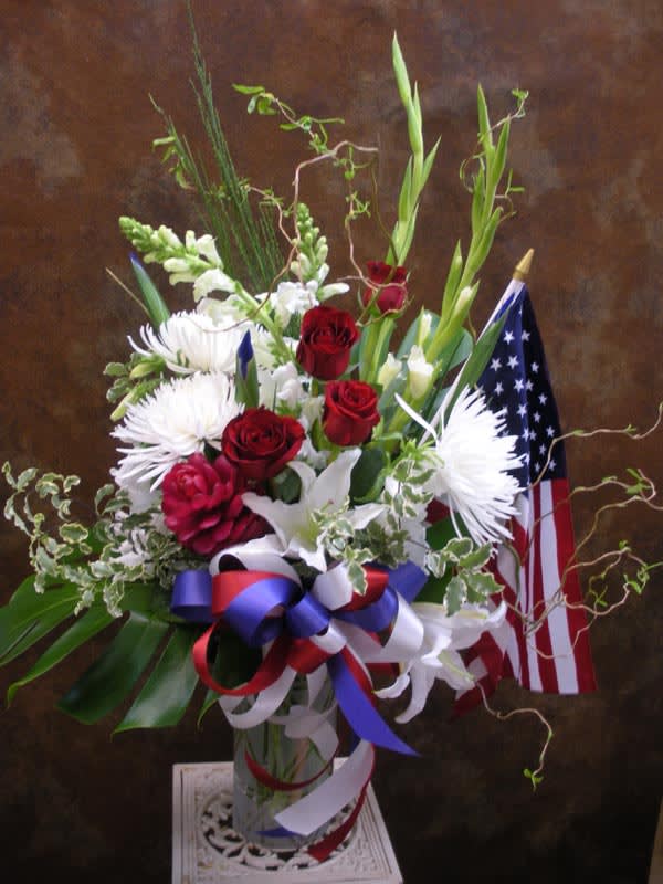 Patriotic Sympathy (SY-0) - Lilies, Gladiolas, Roses, Spider Mums, Irises &amp; more in a glass vase with a bow and flag.