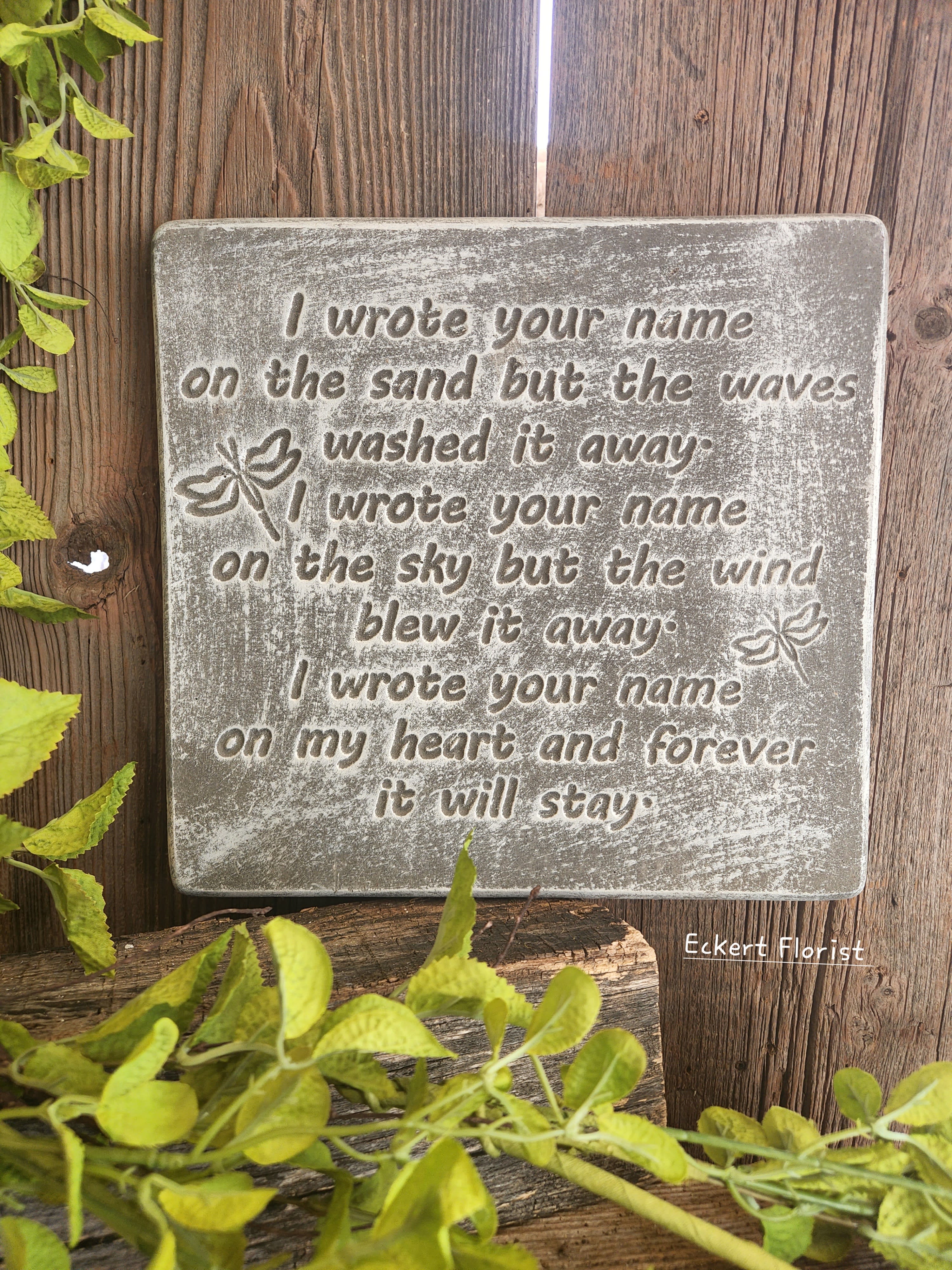 Eckert Florist's "I Wrote Your Name..." Memorial Stone Eckert Florist's "I Wrote Your Name..." Memorial Stone - *Our Local Delivery Only "I wrote your name on the sand but the Waves washed it away. I wrote your name on the sky but the wind blew it away. I wrote your name on my heart and forever it will stay.." Cement Stone measures approx. 11.25" H X 12" W *Stand Included *Upgrade with artificial flowers. See Deluxe option. ALL OF OUR STONES COME DECORATED WITH A SHEER BOW, WILLOW, RAFFIA, AND OUR SIGNATURE BIRD.