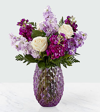 Sweet Devotion Bouquet - Let those know you hold them dear in a truly beautiful way. An array of cream roses and hues of violet stock burst from a lavender glass vase with a diamond pattern and comes together to create an artful collection of flowers. Whether it's a long-distance friend or a family member down the street, this collection of flowers makes for a sweet gift. 