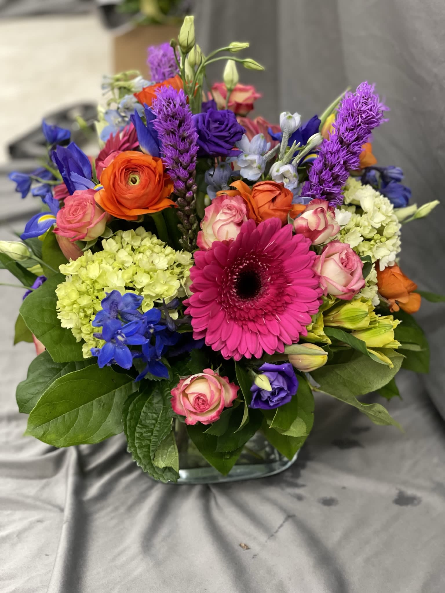 Colorful Celebrations - A mix of vibrant jewel toned seasonal blooms arranged into a sleek, stylish glass cube vase.