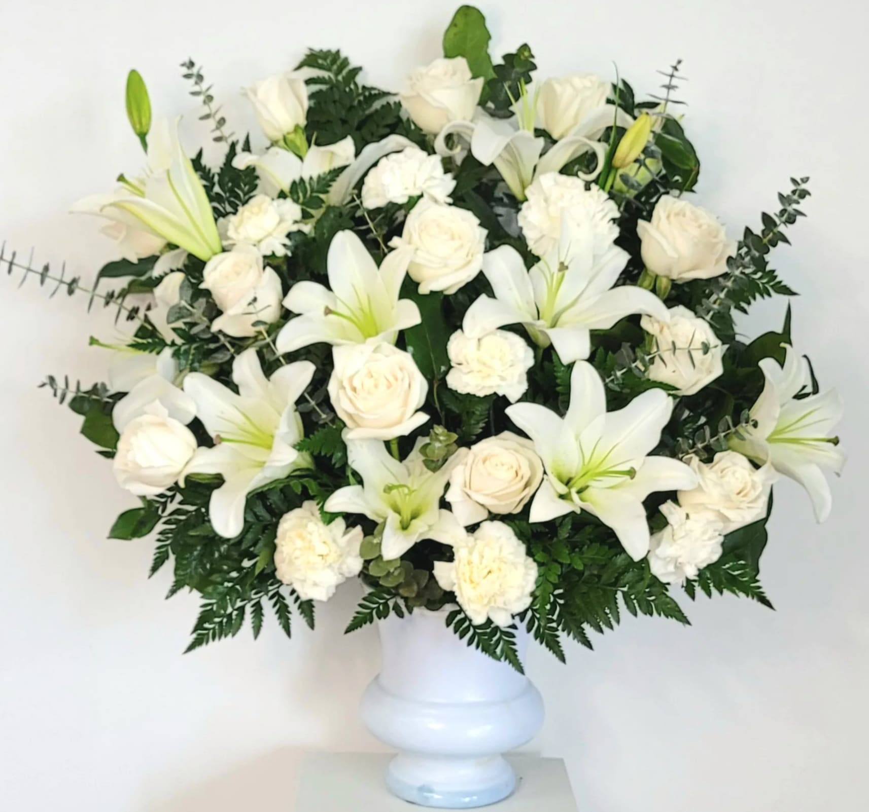 Blessings Above Urn Basket Blessings Above Urn Basket - Several white lilies and beautiful playa blanca roses in a white urn basket.