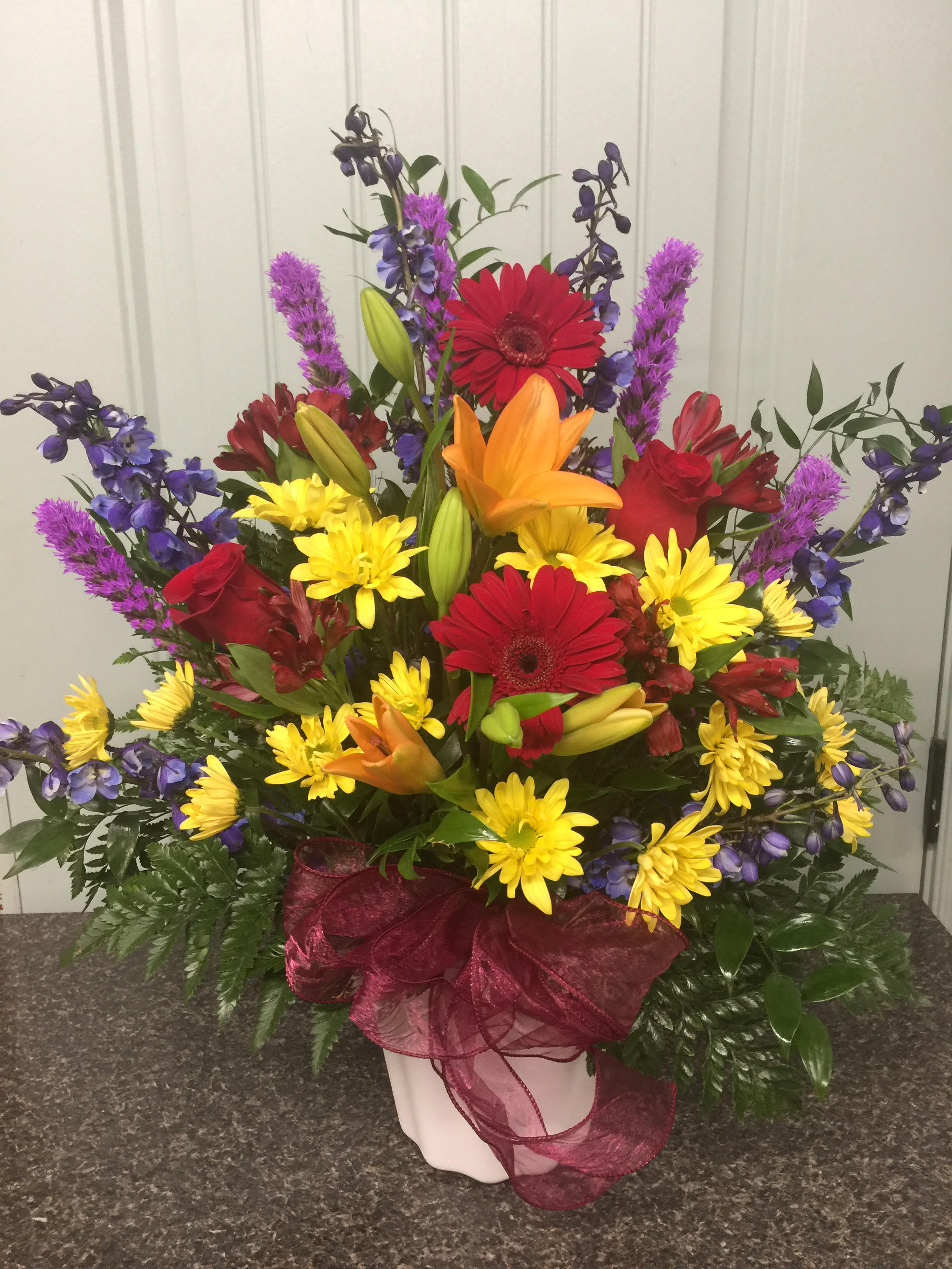 vibrate sympathy basket - colorful arrangement with lilies, roses, gerbs, daisy. Colors are blue , orange, red, and yellow