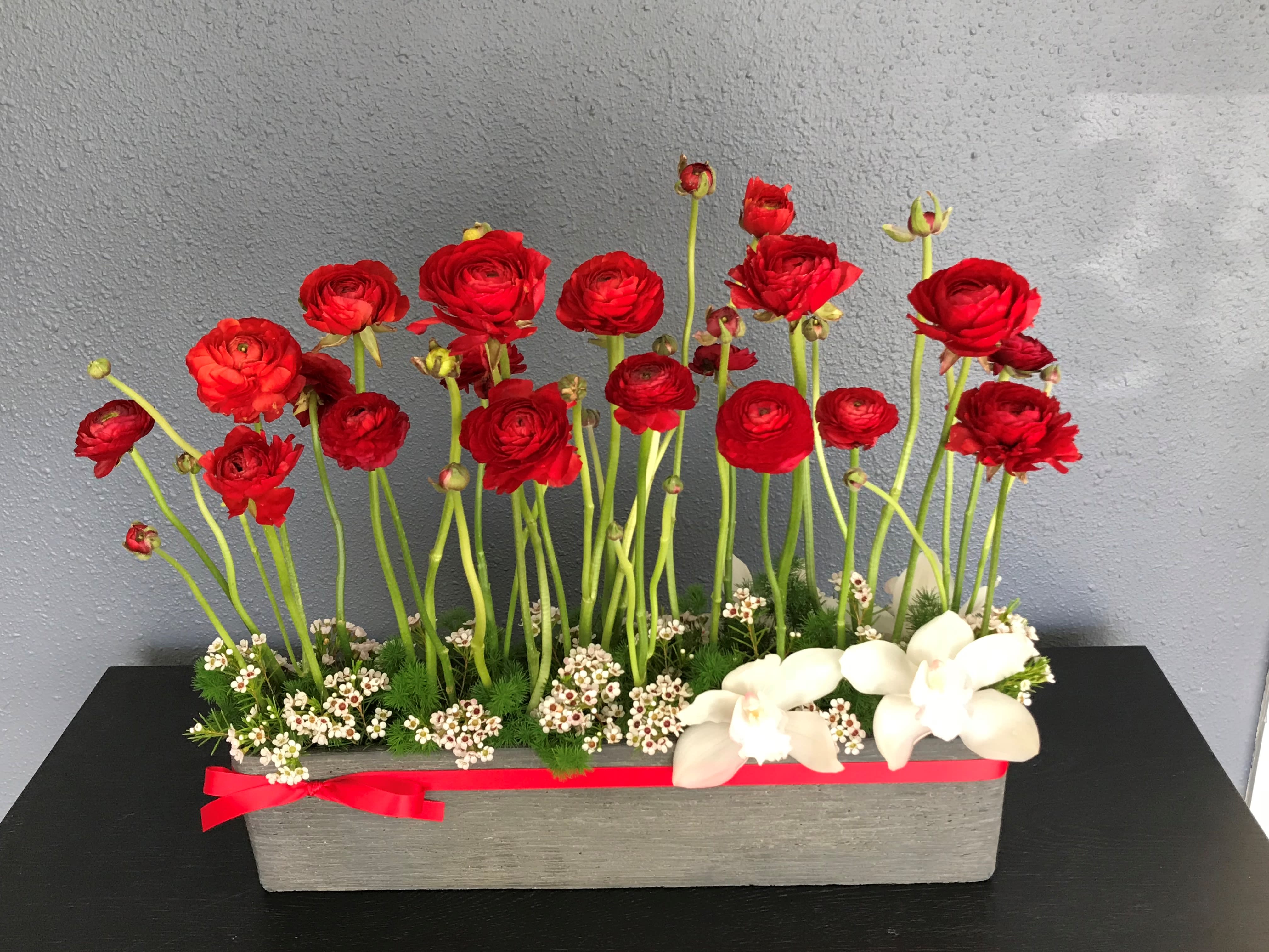 Wonderland - Dimensions:  20L x 18H x 4W  Beautiful red Ranunculus infused with Cymbidium Orchids, Ming greens and Wax flowers in plaster stone vase.