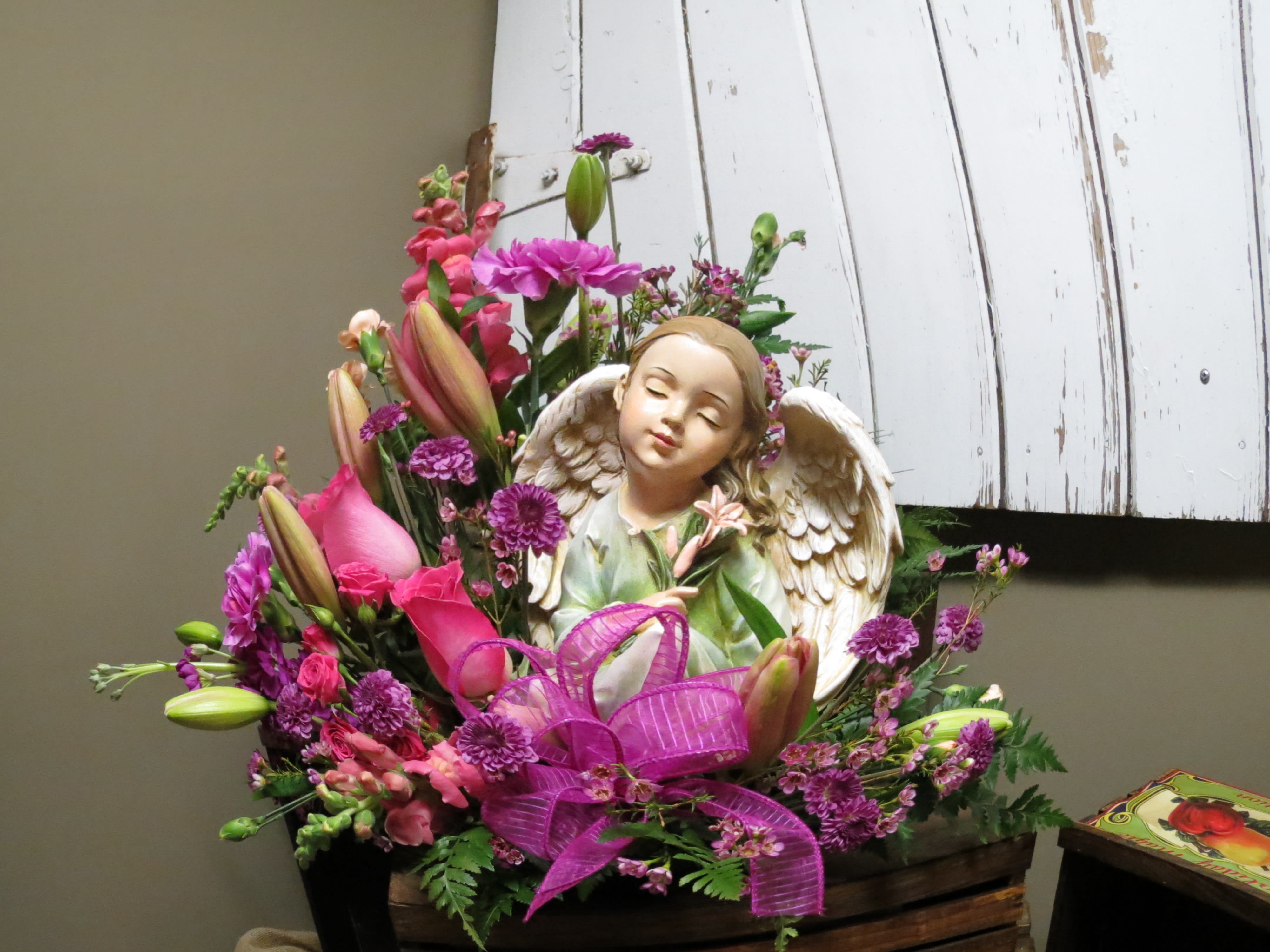 Always Honored Sympathy Custom Design by Cold Spring Floral - Fresh Arrangement with an Angel Resting inside of Pink Roses, Pink Spray Roses, Snapdragons, Purple Mums and Purple Wax flower, Pink Asiatic Lilies, Pink Miniature Carnations, Hot Pink Stock and mixed greenery. Flower variety and statues available may vary. 