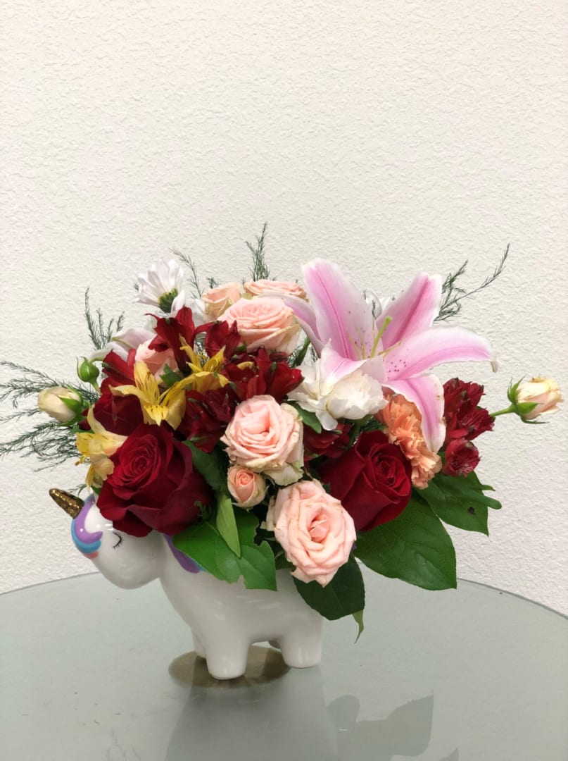 EMELY'S MAGICAL GARDEN - &quot;Nothing’s sweeter than this magical rose bouquet, carefully arranged in this charming, hand-painted ceramic unicorn keepsake!  Peach roses, pink spray roses, white alstroemeria, peach miniature carnations, blue Sinuata statice, and pink Wax flower are accented with huckleberry and pitta Negra. Delivered in a Charmed Unicorn Keepsake.  Orientation: All-Around All prices in USD ($)&quot;