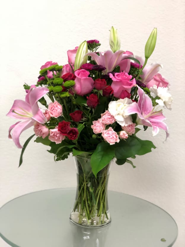 IMPRESS HER - &quot;This fabulously feminine bouquet features hot pink roses, hot pink spray roses, pink Asiatic lilies, pink spray roses, red spray roses, pink carnations, green button spray chrysanthemums, bupleurum, huckleberry and lemon leaf.Delivered in a clear glass Gathering  vase.  SET: One-Sided All prices in USD ($)&quot;