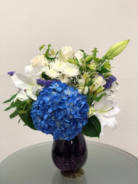 Blue hydrangea and white lily bouquet in a dark glass vase