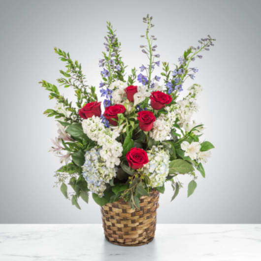 Forever Remembered by BloomNation™ Forever Remembered by BloomNation™ - A red, white, and blue tribute funeral basket featuring red roses, blue hydrangea, blue delphinium, and white stock. Fitting for any type of funeral ceremony.