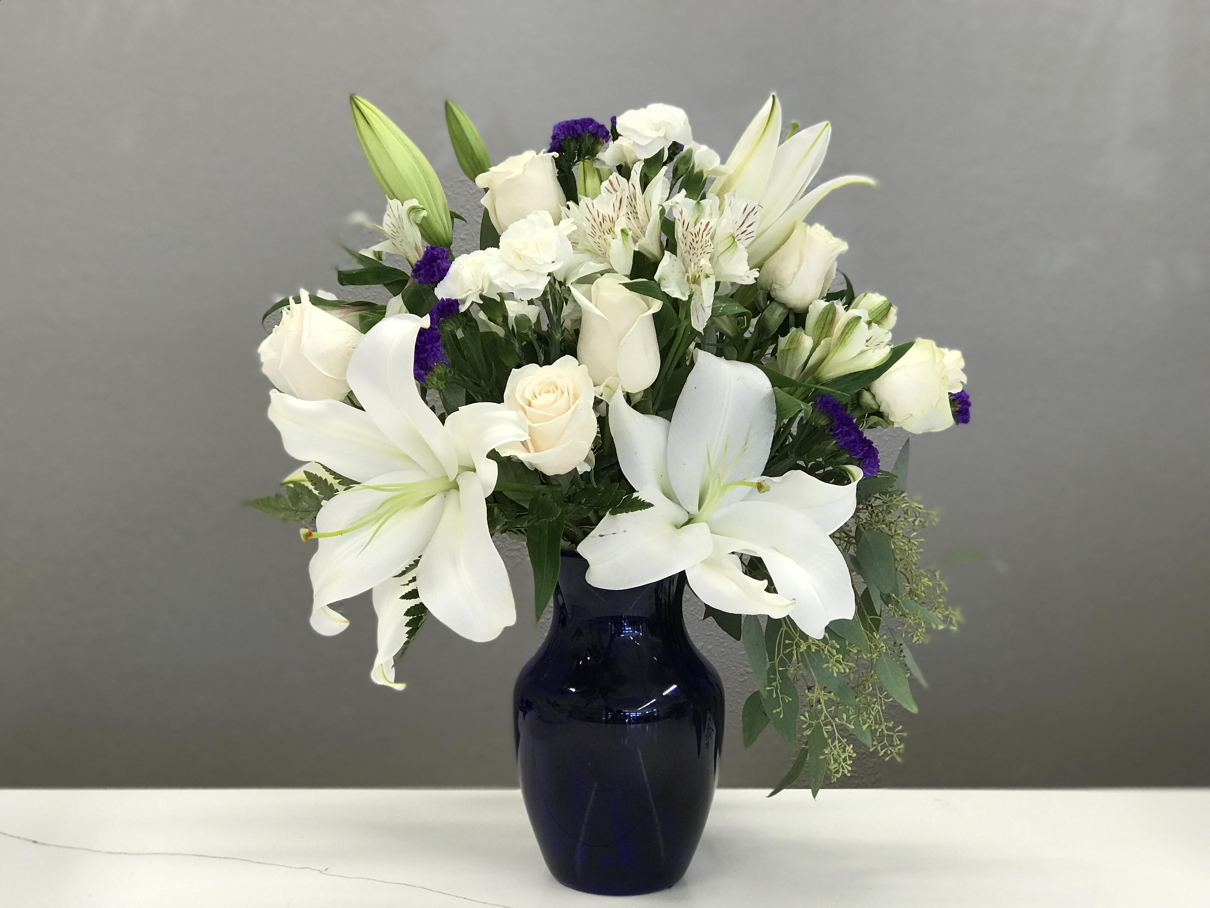 Cherished Always - Beautiful white lilies surrounded by cream roses and bursts of purple statice to remind friends and family they're on your heart. 