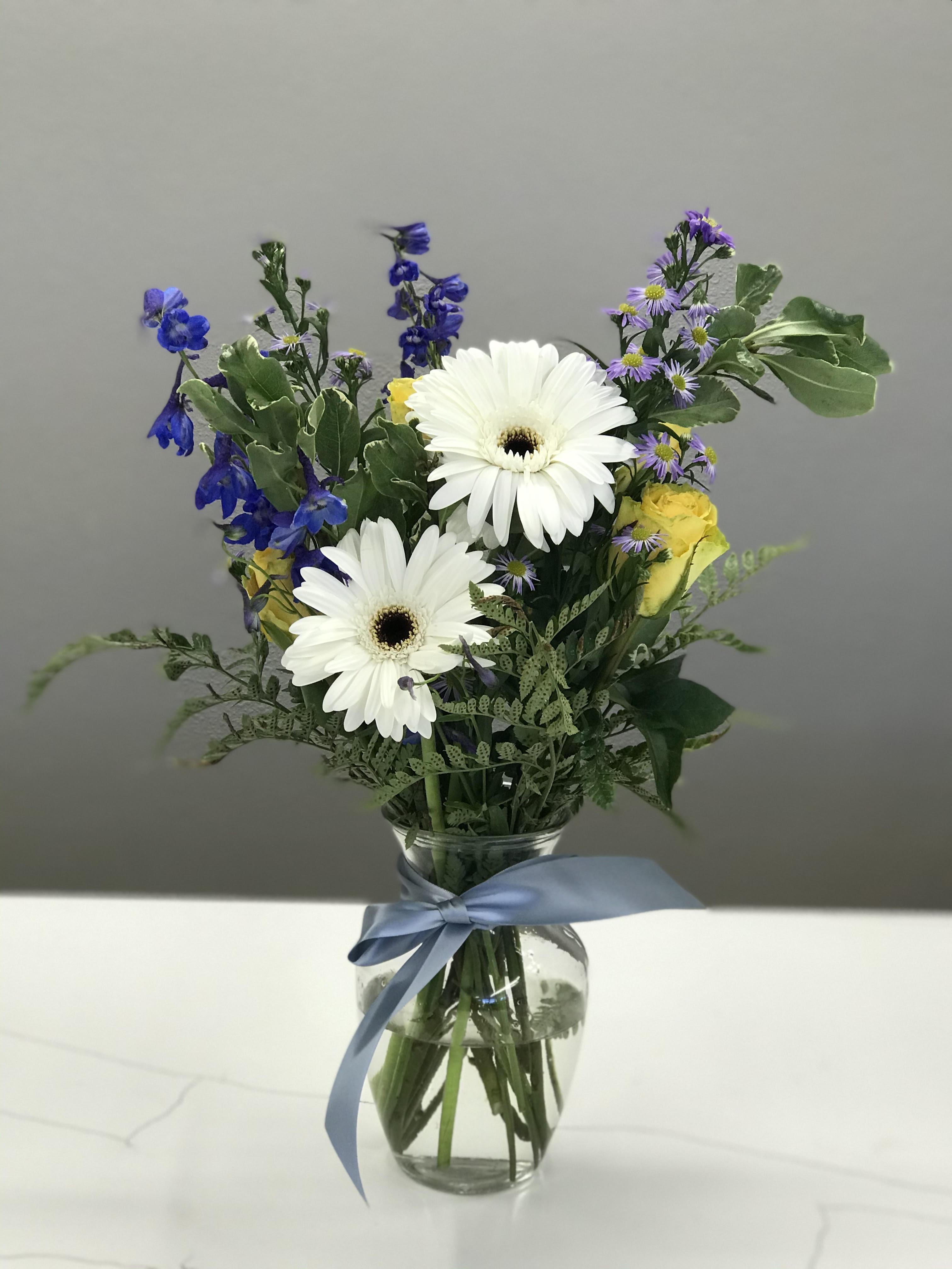Double Scoop - Two dollops of Gerbera daisy nestled in yellow roses and blue delphinium for a tendered hearted hello. Perfect for a celebration of life, birthdays, or healing thoughts. 
